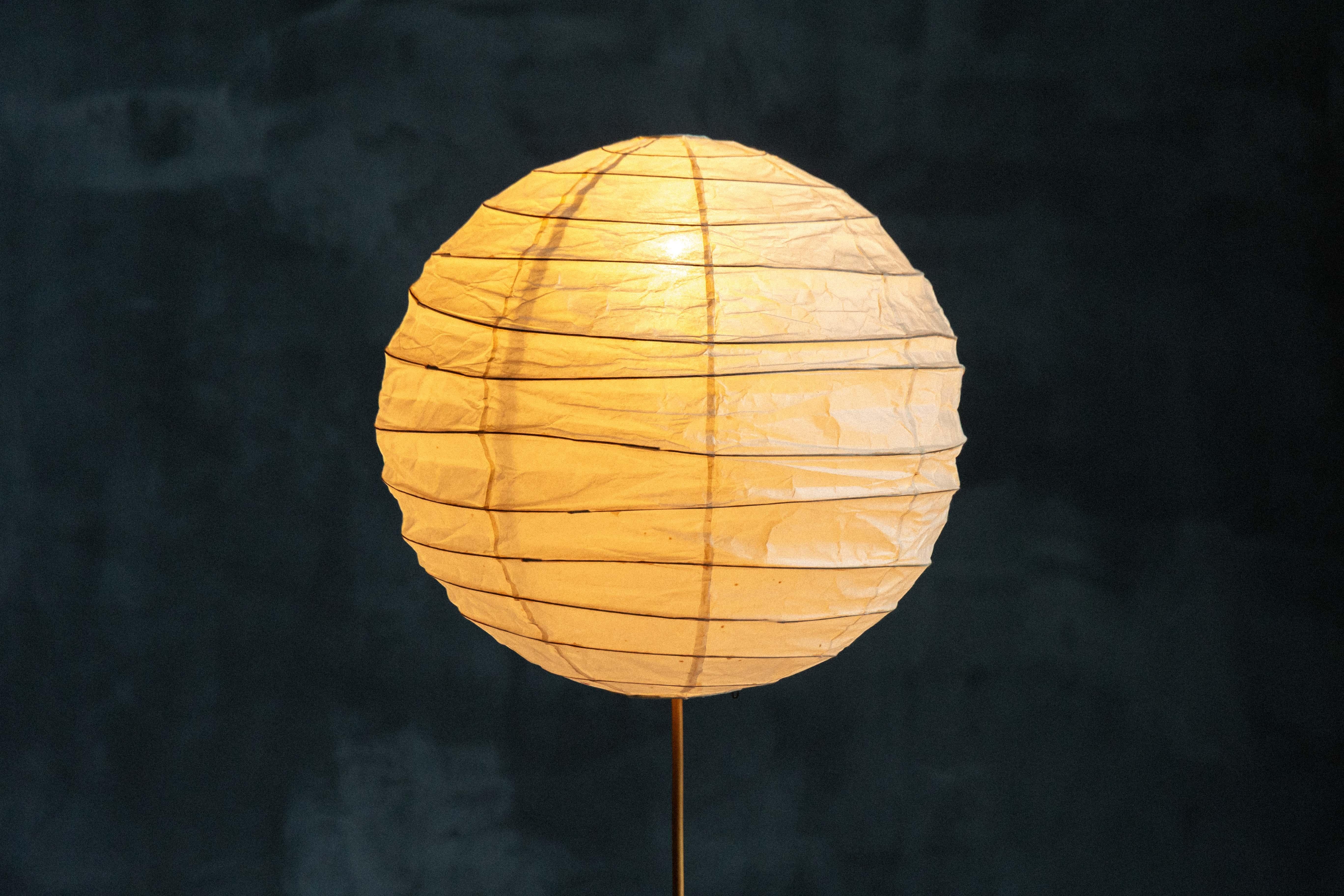 Esta lámpara de pie Akari de Isamu Noguchi, excepcionalmente rara, tiene una elegante pantalla en forma de globo elaborada con papel washi hecho a mano, procedente de Gifu (Japón), famosa por su fina artesanía en papel. A diferencia de las lámparas