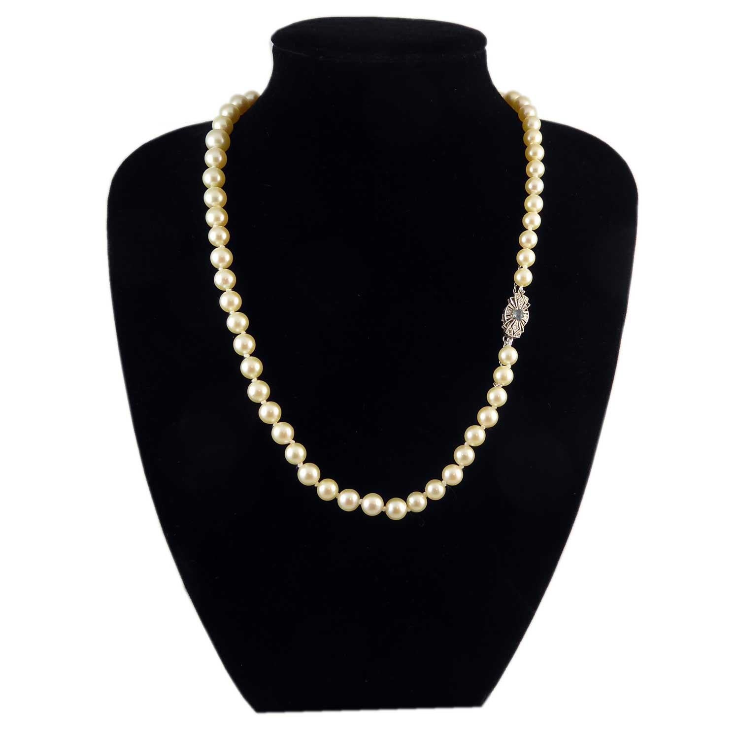 A single row of Akoya cultured pearls comprising 61 off-round cultured pearls of light to medium cream colour.  The pearls graduate in size from 6.78mm to 9.44 and are threaded knotted to a decorative oval bow plaque style snap which may be worn at