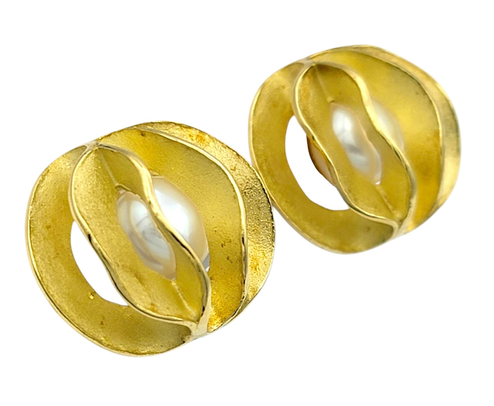 Ces boucles d'oreilles modernistes présentent une fusion frappante de texture et de forme, réalisée en or jaune 18 carats avec une finition sablée audacieuse. Le design sculptural encadre une perle de culture Akoya d'un blanc éclatant au centre de