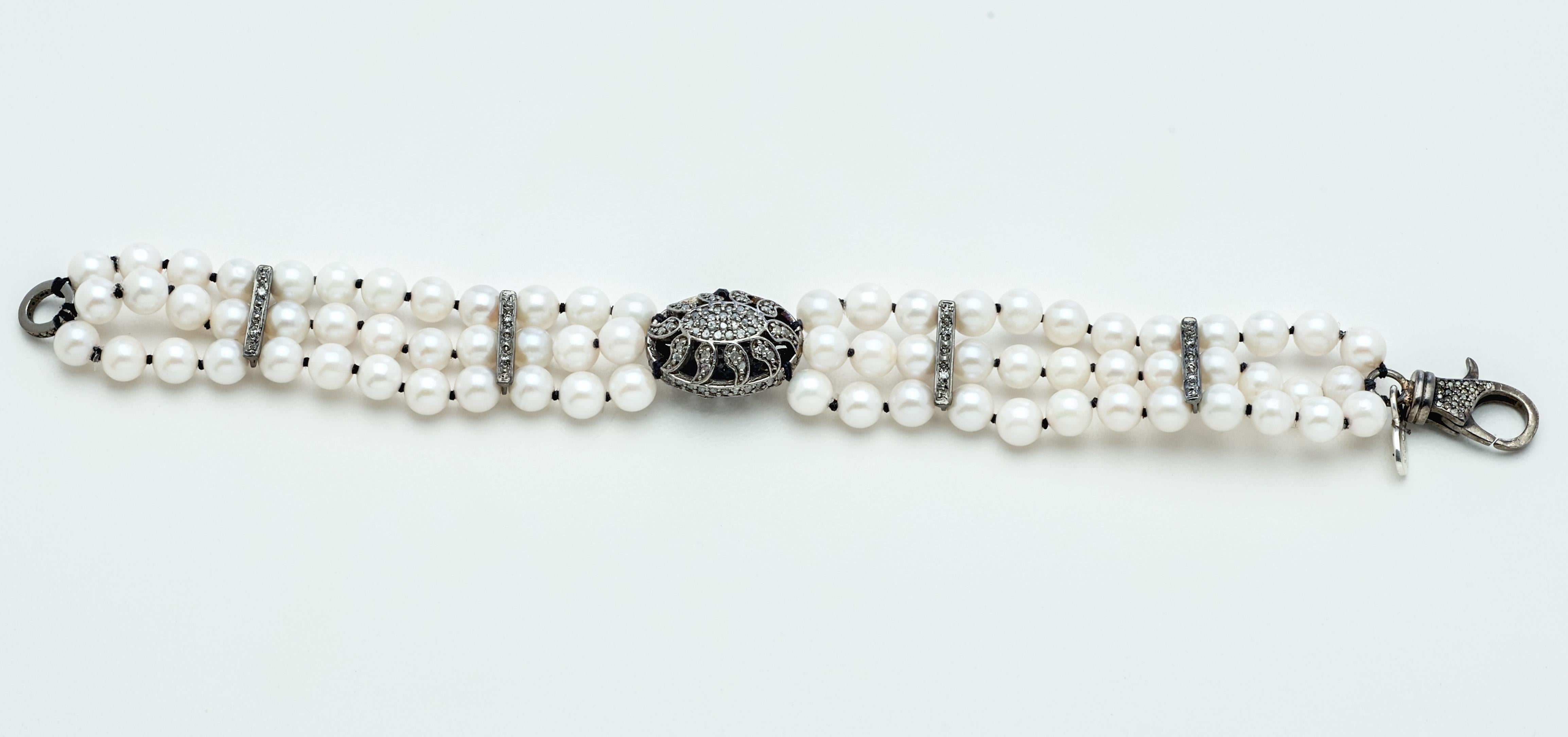 A vintage style diamond puff charm crowns three strands of lustrous 5-1/2mm x 5-3/4  AAA white round Akoya pearls to create this very attractive and unique new artisan bracelet. Matching diamond sterling silver bars and a fancy diamond silver clasp
