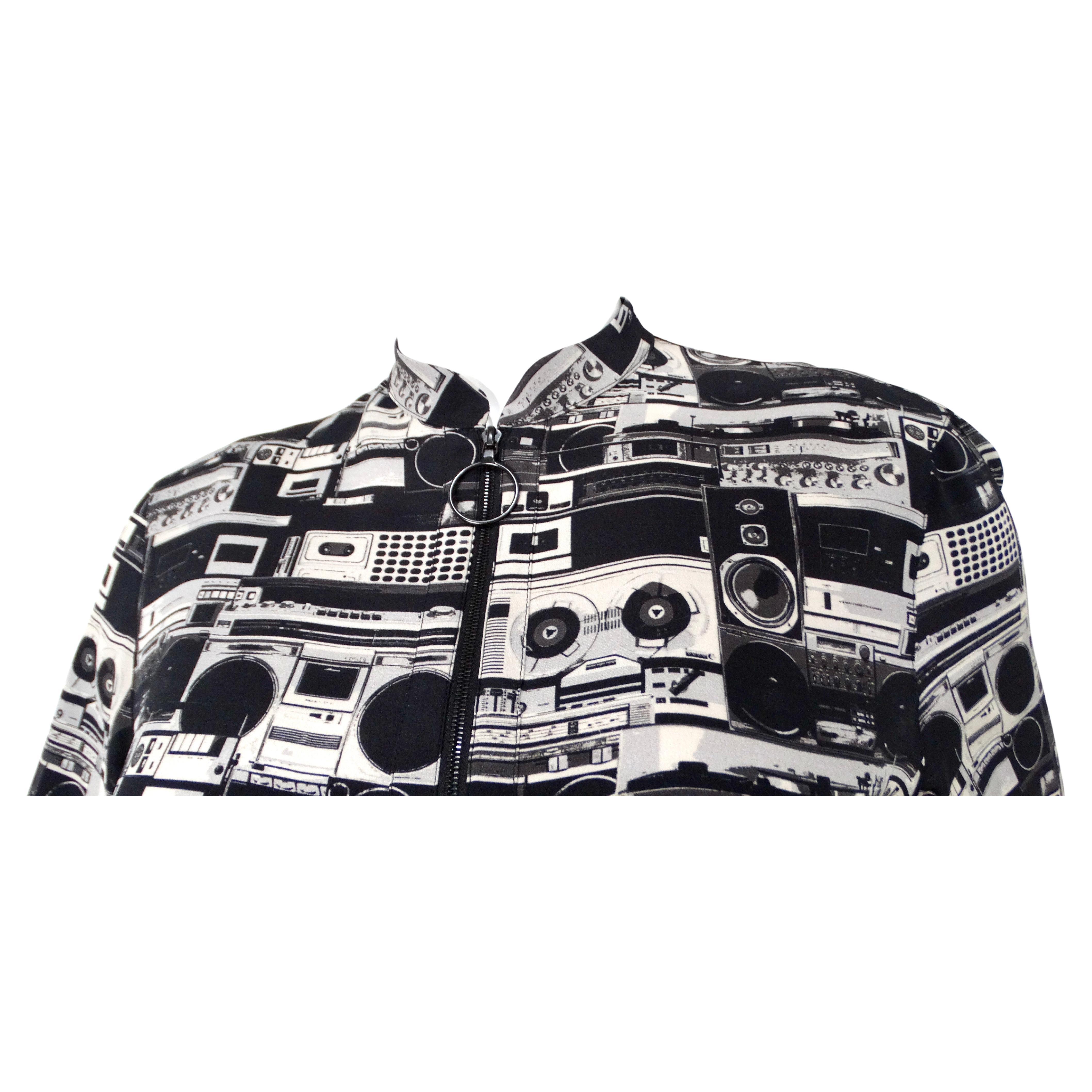 La blusa Akris Punto Stereo Print Half-Zip è un pezzo sorprendente e contemporaneo che fonde perfettamente la stampa artistica con il tessuto di lusso. Realizzata in seta liscia, questa blusa presenta una stampa stereo all-over in nero e grigio che
