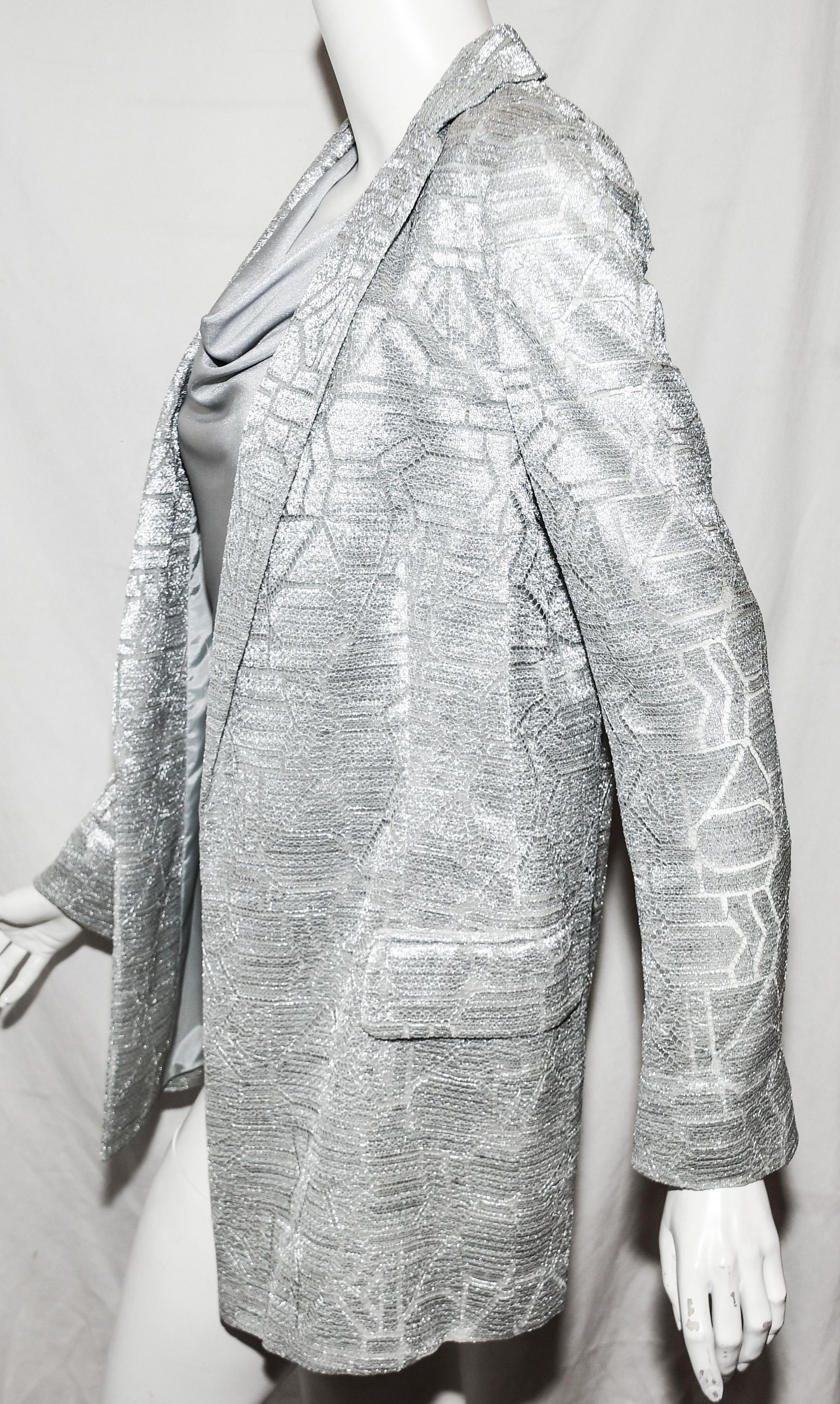 Akris silver tone lace in an abstract modern design but incorporating classic undertones. This
jacket contains a notched collar and turn up cuffs.  It is fully lined in silver Mulberry silk.  This garment is to be worn open at front.  Two flap