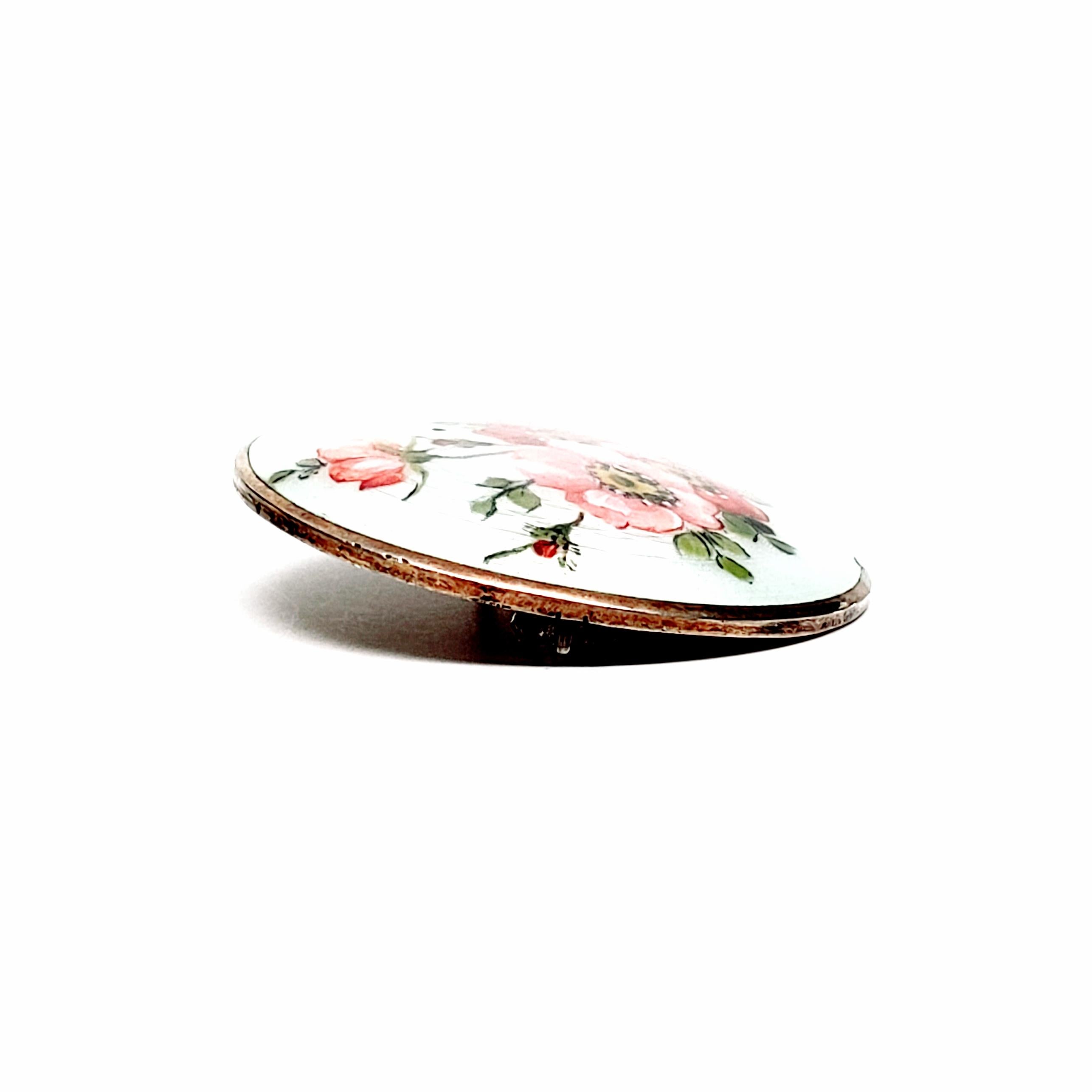 Gold vermeil over sterling silver round enameled pin with flowers by Aksel Holmsen, circa 1950s.

Beautiful white guillouche enamel painted with pink flowers and green leaves.

Measures approx 1 1/2