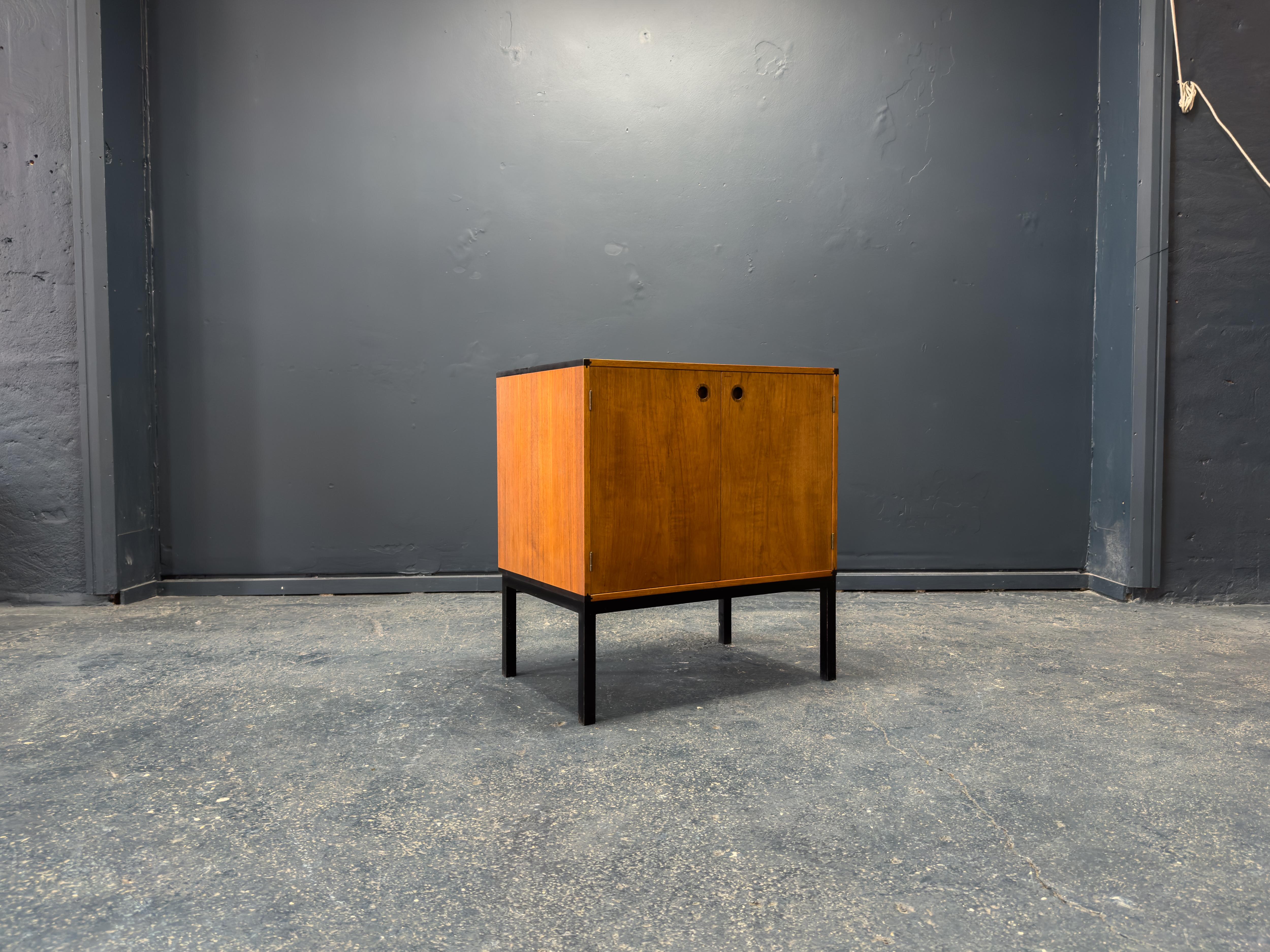 Ce meuble en teck carré raffiné d'Aksel Kjersgaard est un chef-d'œuvre de design minimaliste et d'artisanat expert. Reposant sur d'élégants pieds en métal noir, la pièce acquiert une subtile touche industrielle, qui contraste magnifiquement avec la