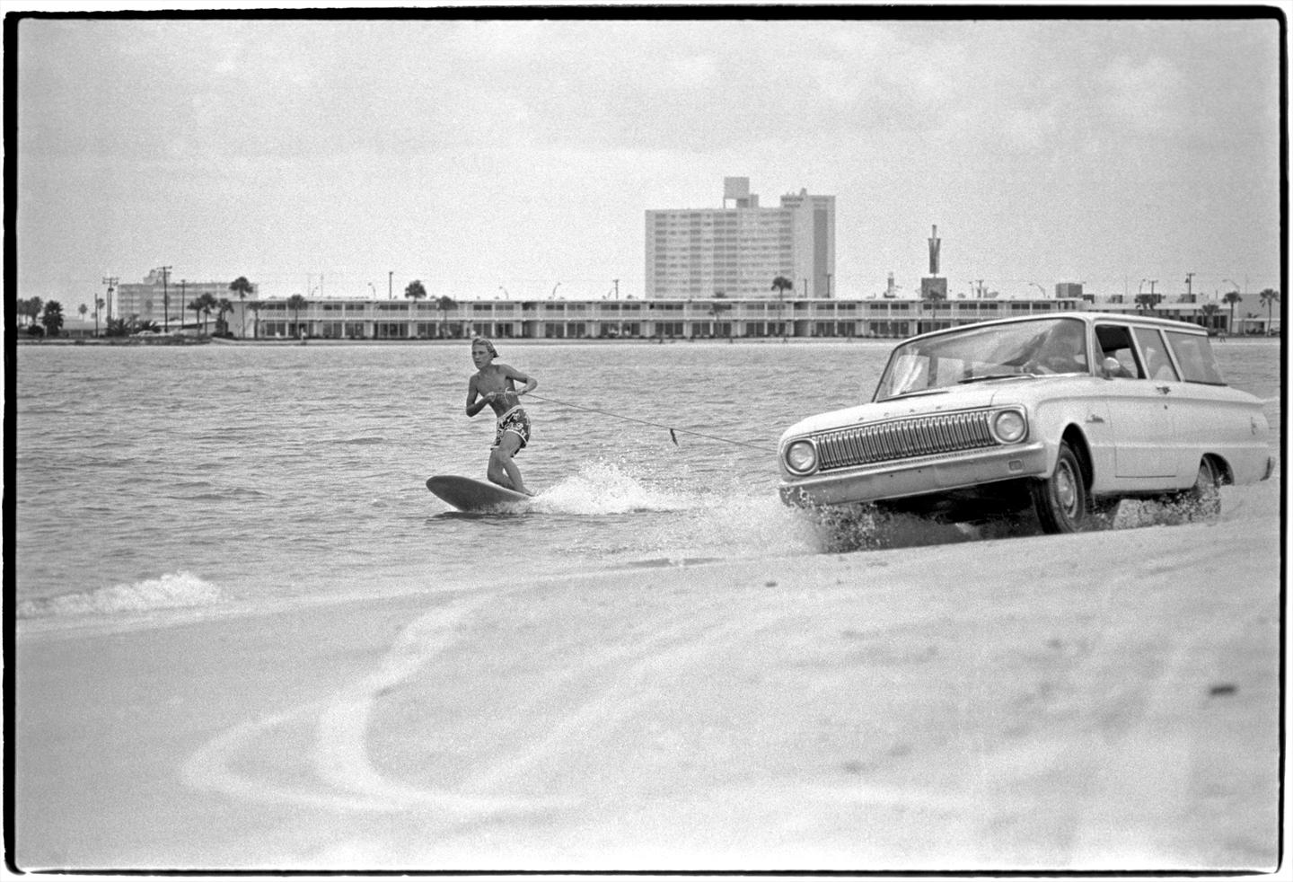 Catching a Ride by Al Satterwhite is a 11 x 14 inch archival pigment print, available in an edition of 25. This photograph features a man surfing in the ocean while being pulled by a car driving on the sand.
This photograph is signed with edition