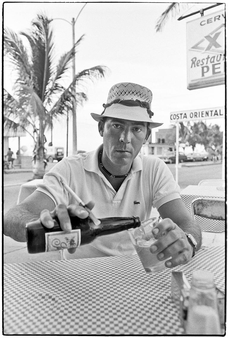 Hunter S. Thompson in Cozumel by Al Satterwhite features a portrait of Hunter S. Thompson sitting at a table while pouring a beer into a glass.

This photograph is listed as a 17.75 x 12 inch archival pigment print, with the paper size measuring 20