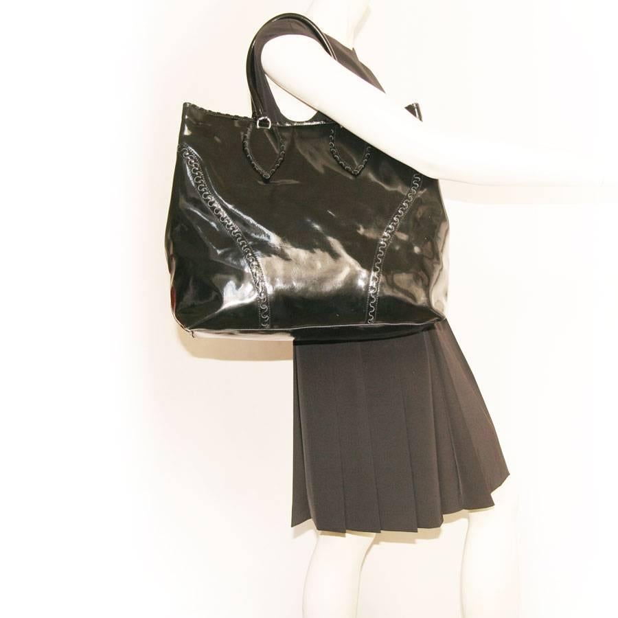 Alaïa Large tote bag in black patent leather. The hardware is in silver metal.
Worn by hand or arm with two handles that each measure 46 cm.  The interior is in leather with three pockets: one zipper, one that closes with a pressure and a flat