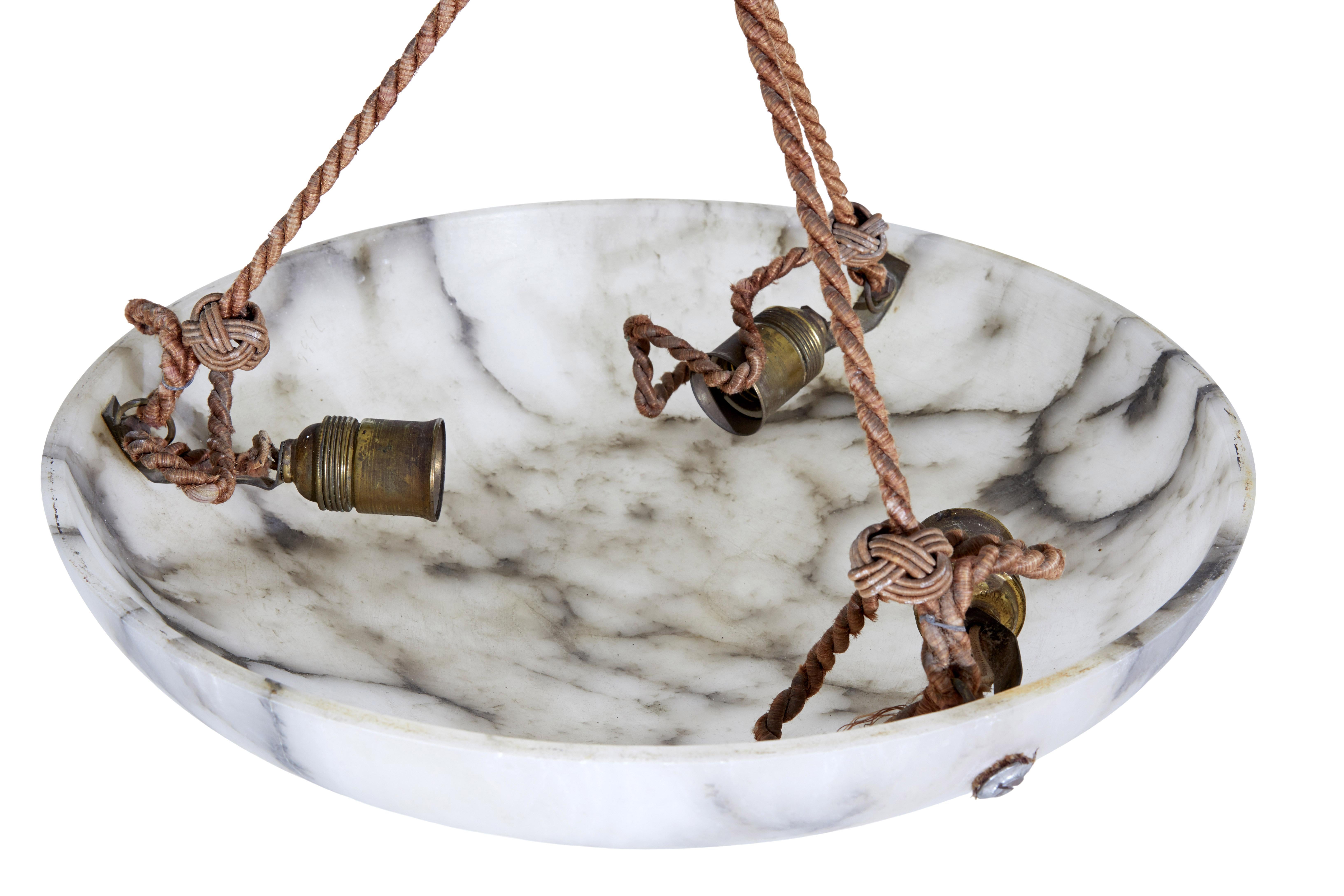 Alabaster art deco ceiling light circa 1920.

Good quality swedish alabaster dish light, made from warm whites/greys with darker grey veining.  Light is suspended by 3 ropes that lead up to a latice strung ceiling rose.

The light is fitted with