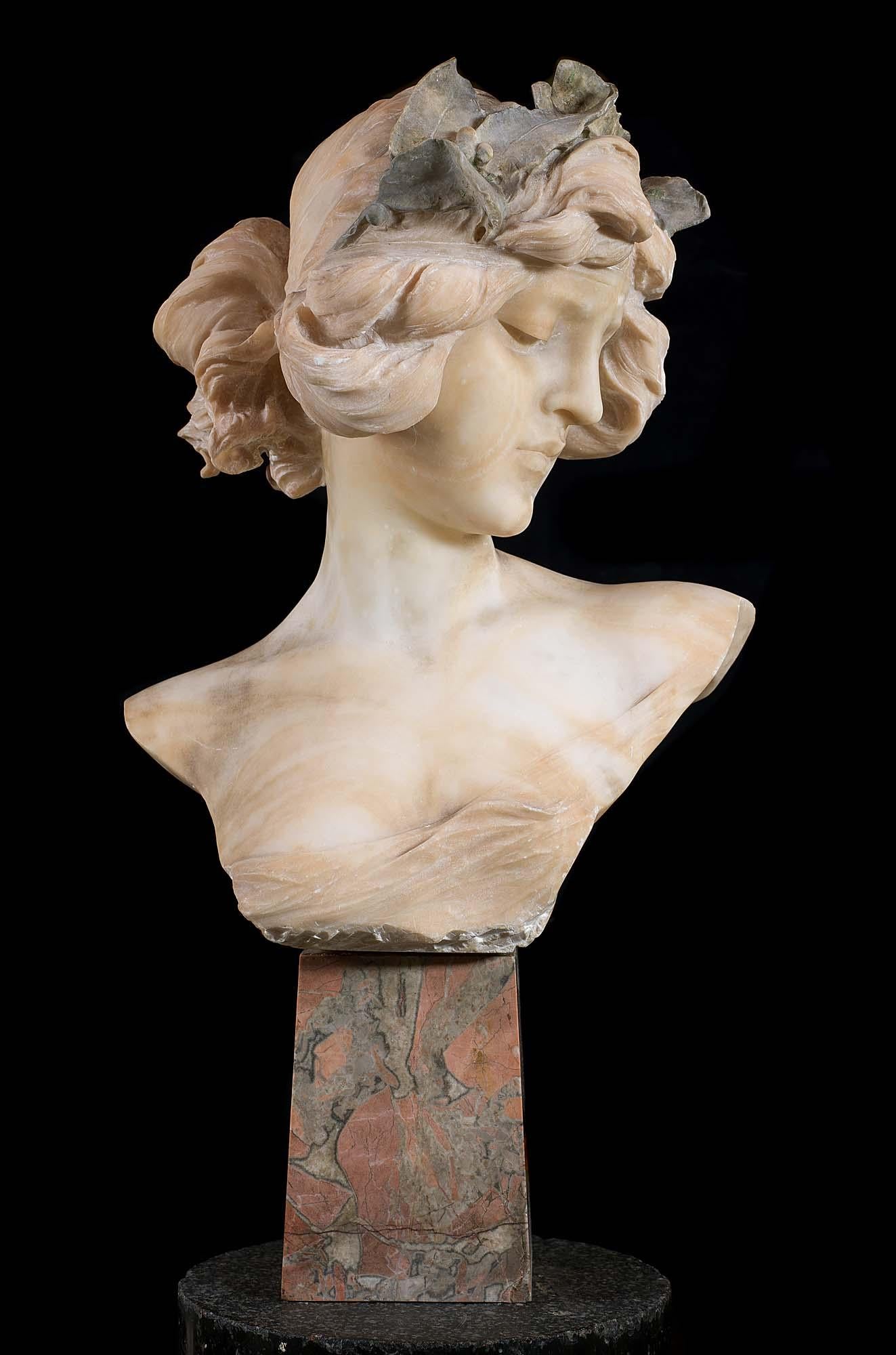 A charming and finely carved Alabaster bust of an Art Nouveau woman with demurely downcast cast eyes. Her casually elegant hairstyle is adorned with an entwined leaf wreath and she is raised on a rouge and grey marble base. English, late 19th