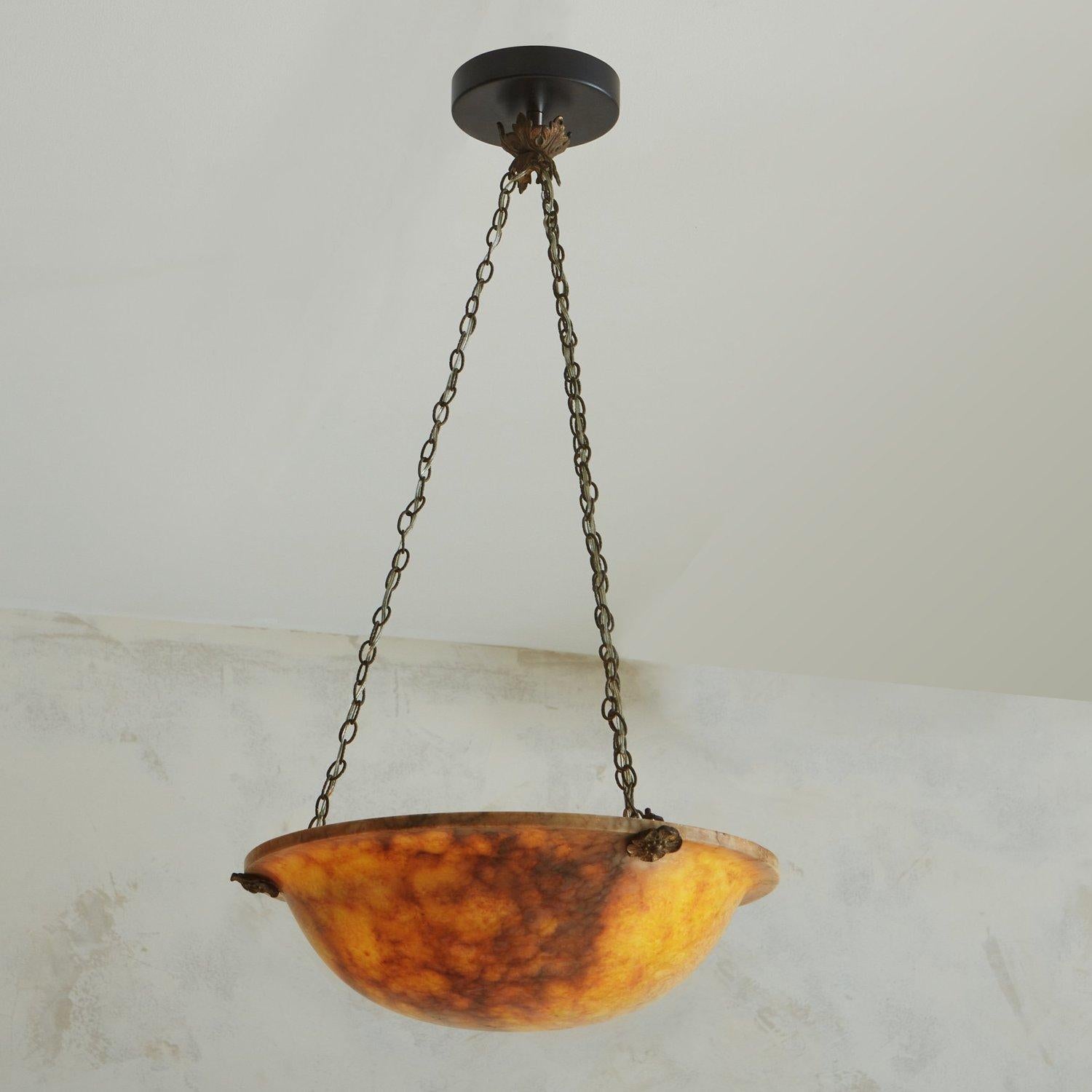 An elegant 1960s French pendant light featuring an alabaster shade in a lovely orange hue with gray and cream veining. The shade is suspended from three bronze chains, which attach to the dome and canopy with bronze rosette hardware. This pendant