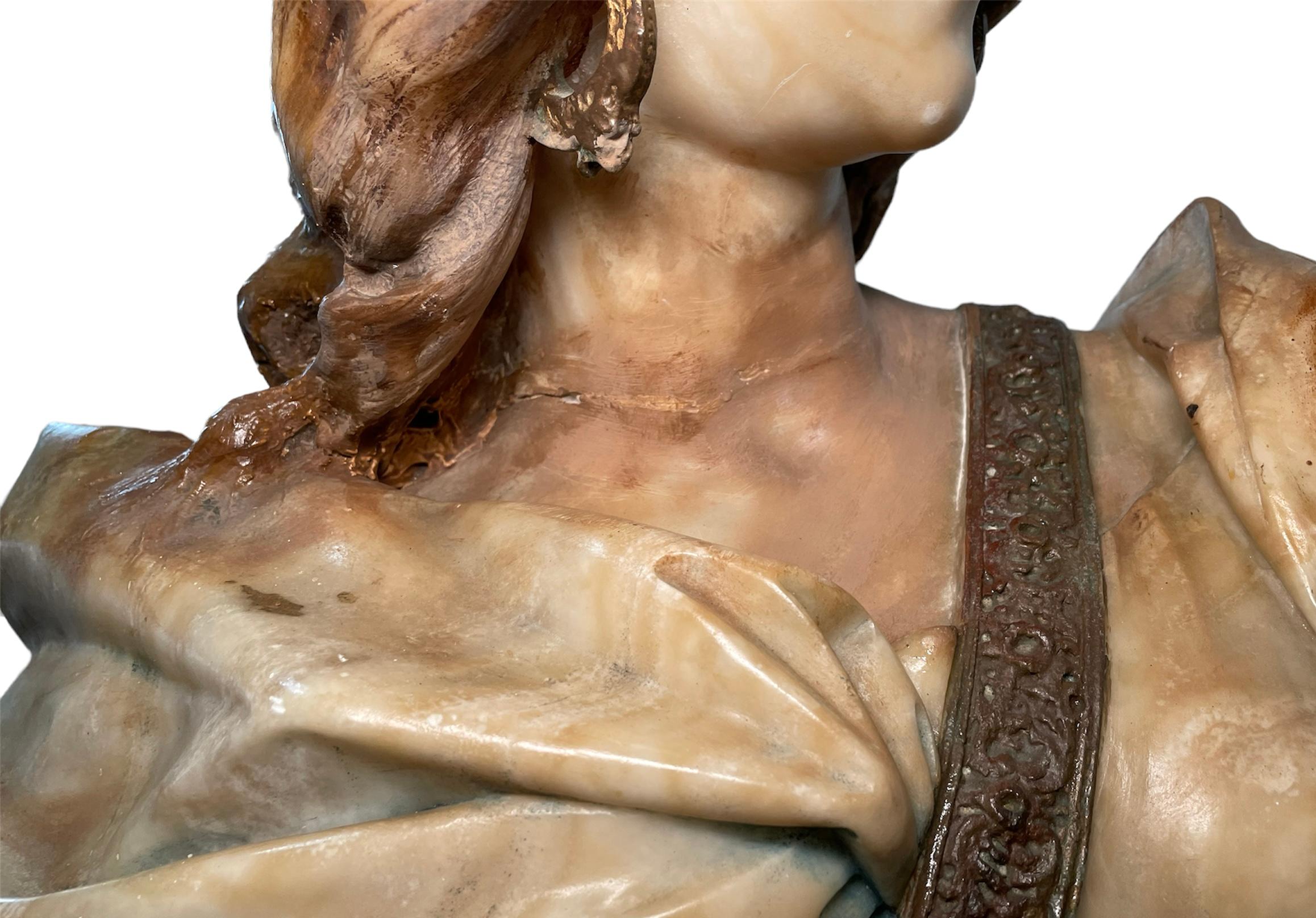 This is a heavy alabaster bust sculpture of Judith after the painting of August Riedel. It depicts the bust of a light brown wavy hair female who is wearing a beige robe that is hold by a leather belt that holds a sword in the center of her chest.