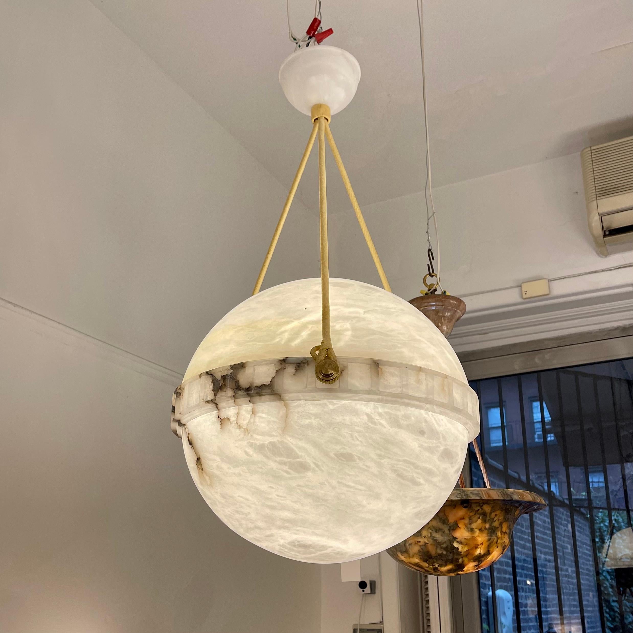 Carved from a single block of alabaster stone, primarily white with dark black veinings running through both hemispheres. Features a matching canopy, and currently mounts one 75W max LED bulb. Rewiring to your specificied drop is included in the