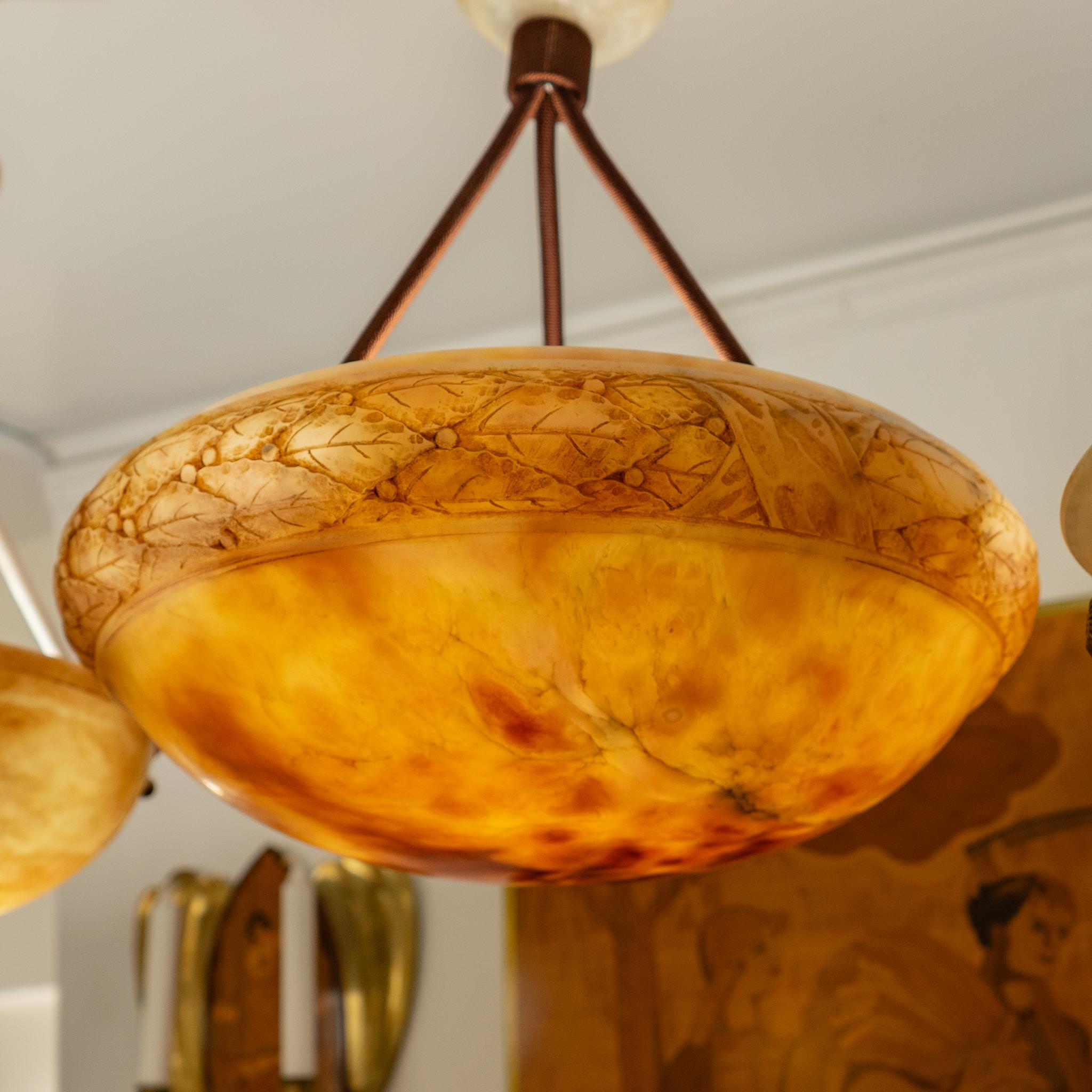 Les tons chauds de l'ambre se mêlent à un anneau de feuilles de laurier sculptées.  La minéralisation est présente dans l'ensemble de ce luminaire en pierre d'albâtre, ajoutant de la profondeur et de la chaleur à la lumière diffusée par trois