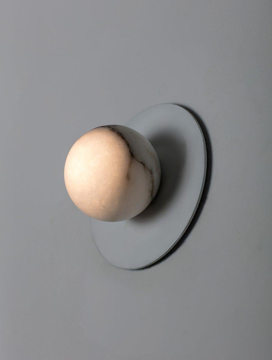 Un globo de alabastro se asienta a ras sobre un disco de latón fundido. El hardware desaparece y la esfera se vuelve misteriosamente infinita.
