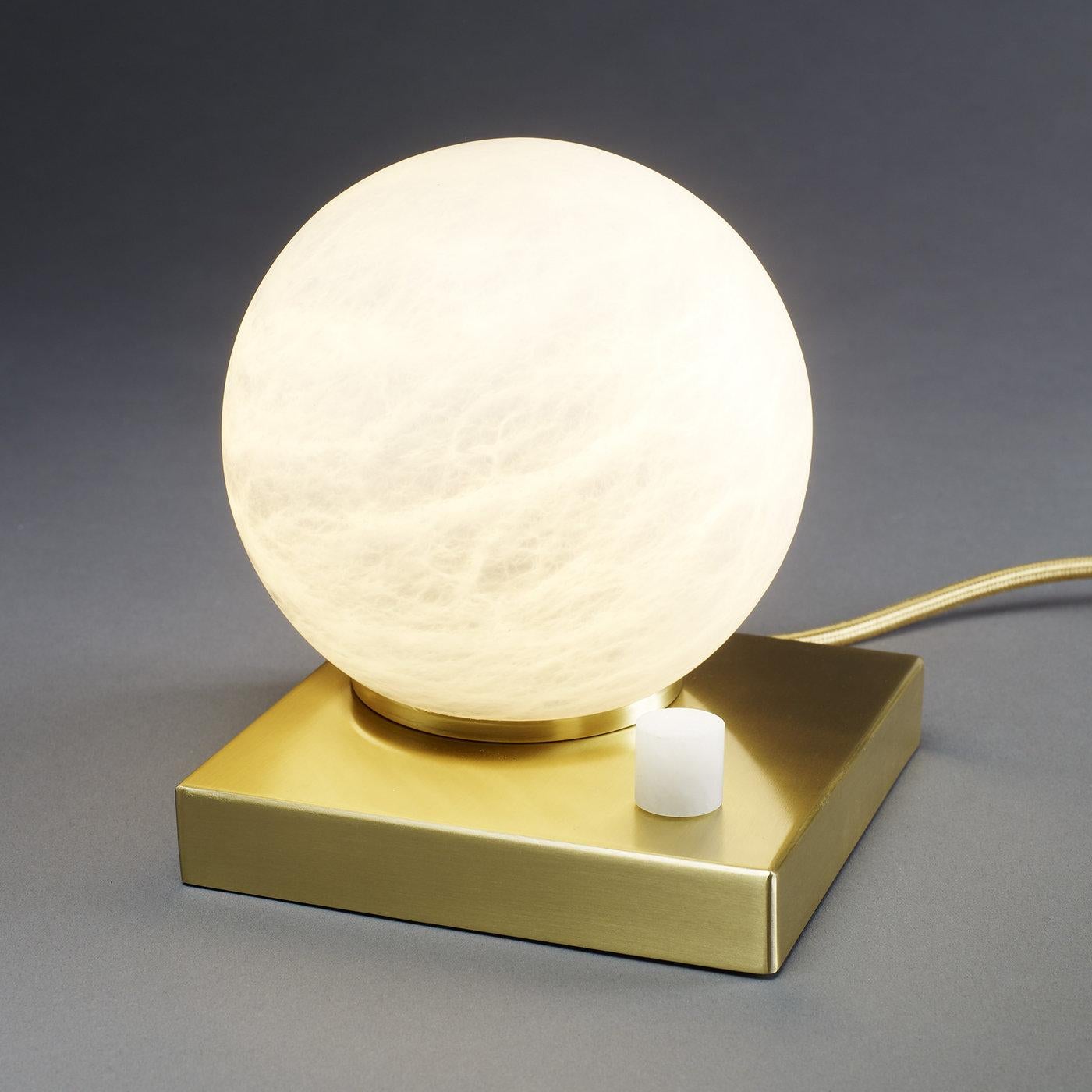 A magnificent table lamp of undeniable allure, this sculptural masterpiece features a dimmable and soft light, whose warm temperature is reflected by the spherical diffuser in alabaster, showcasing its natural grain and translucent surface. The base