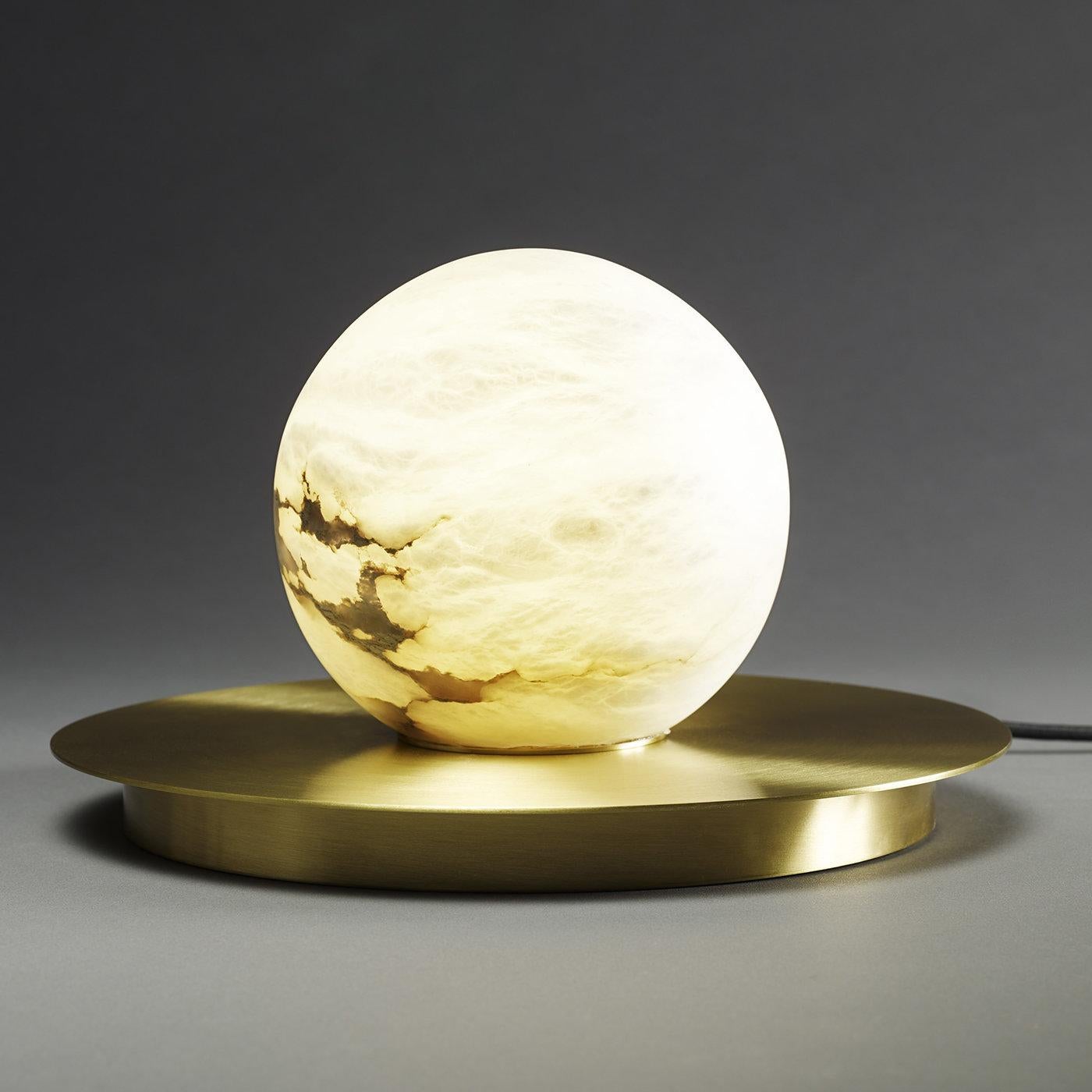 Translucent and warm, the surface of this elegant alabaster globe with stunning veining is lit from within, creating the magical effect of a full moon. The polished brass disk that serves as a base adds evocative reflections to this stunning table