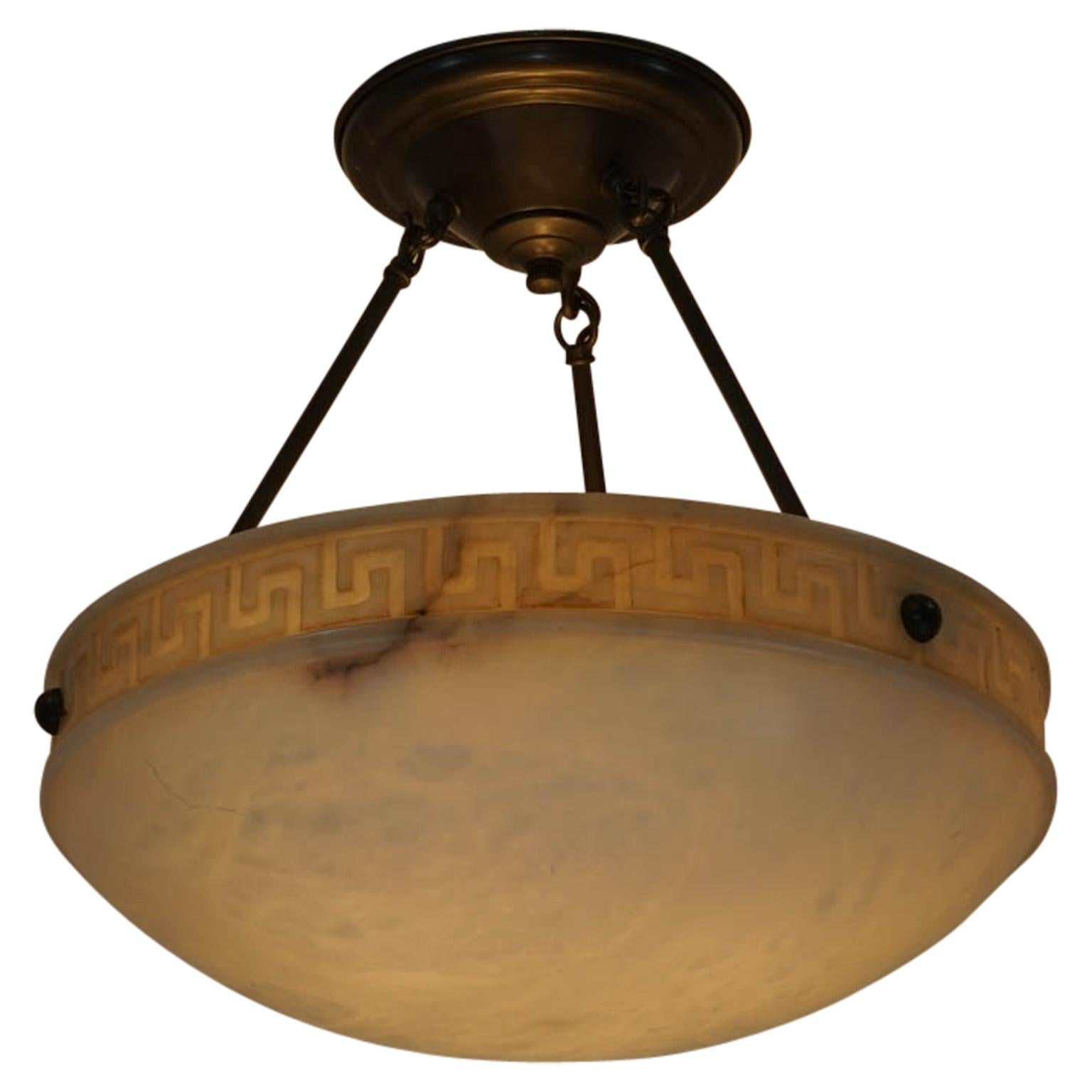 A warm white alabaster shade is suspended from three rods. A stylized Greek key has been carved into the upper rim of the shade.