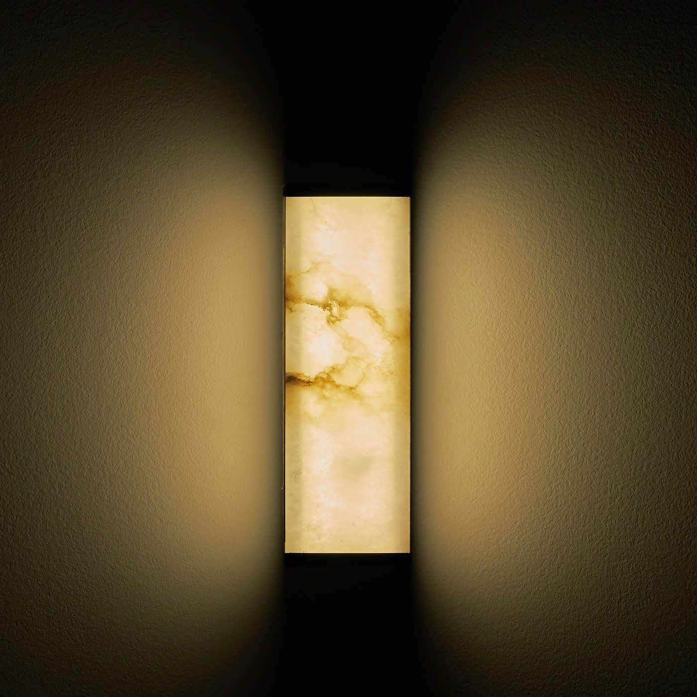 The Tech short wall sconce was conceived with the idea of merging the luminaire with the lampshade into a single element, playing on the transparencies of the light through the ultra-thin alabaster encased in a satin brass frame with a simple linear