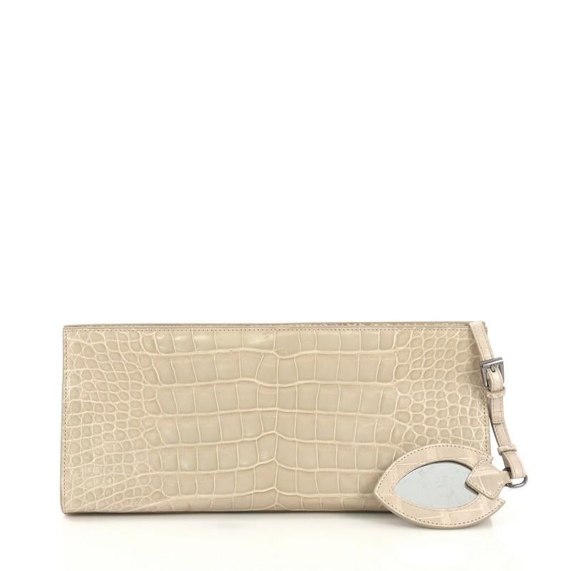 This Alaia Clutch Crocodile Long, crafted from genuine neutral crocodile skin, features gunmetal-tone hardware. Its magnetic closure opens to a neutral leather interior with side slip pocket.  This item can only be shipped within the United