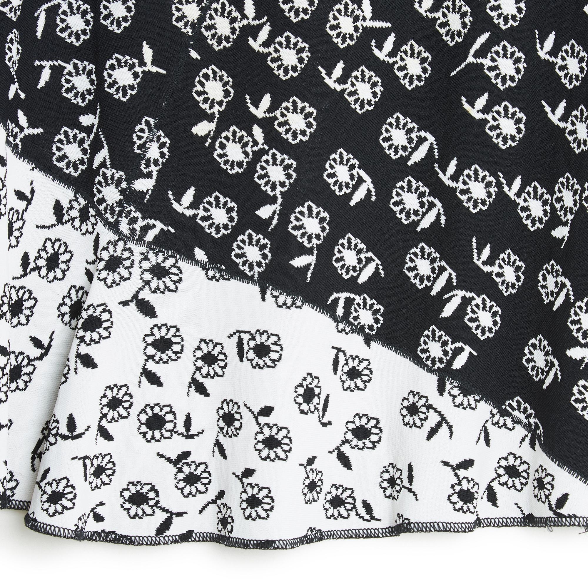 Jupe droite Alaïa en maille douce de viscose mélangée, motif de petites fleurs contrastées en noir sur blanc et blanc sur noir, ceinture montée sur un mini ruban et fermée par un crochet et un zip, non doublée, légèrement plus courte sur le devant.