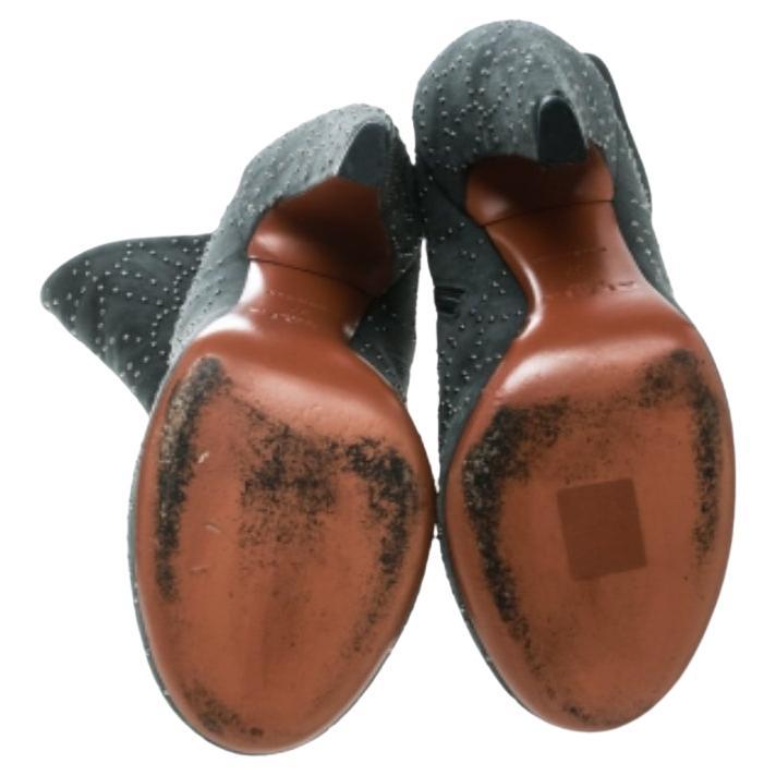 Estas espléndidas botas de Alaia tienen un aire moderno con toques de glamour y brillo. El exterior de ante gris adornado con tachuelas en tono bronce de cañón es visualmente atractivo y la forma, con un tacón curvado en bloque de 13,5 cm, ofrece