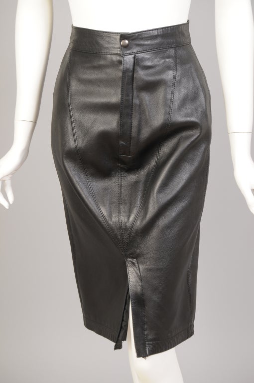 Azzedine Alaia uses soft black leather for this form fitting skirt with double zippers. The skirt has a narrow waistband with a snap above the zipper fly. There is another zipper at the hemline of the skirt, opening up to show more leg. Two elastic