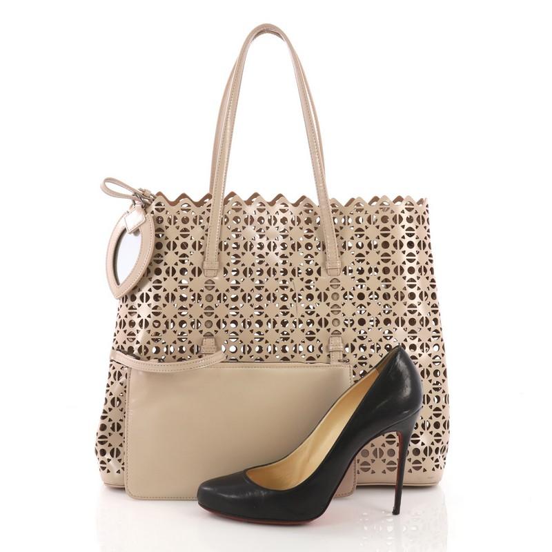 This Alaia Open Tote Laser Cut Leather Medium, crafted in mauve laser cut leather, features jagged edges, tall slim straps, protective base studs, and gunmetal-tone hardware. It opens to a brown laser cut leather interior. **Note: Shoe photographed