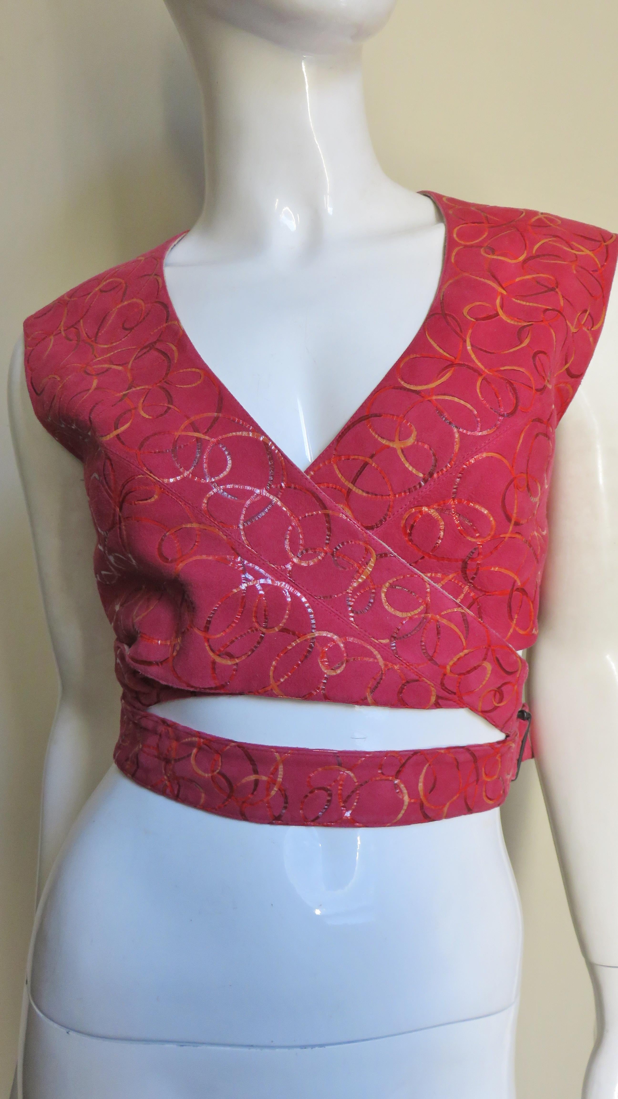 Un favoloso top, un gilet in pelle scamosciata rossa con un sottile motivo circolare di Azzedine Alaia. È senza maniche e si incrocia sul davanti con spalline che si estendono su ogni lato avvolgendo la vita e chiudendosi con una fibbia regolabile.