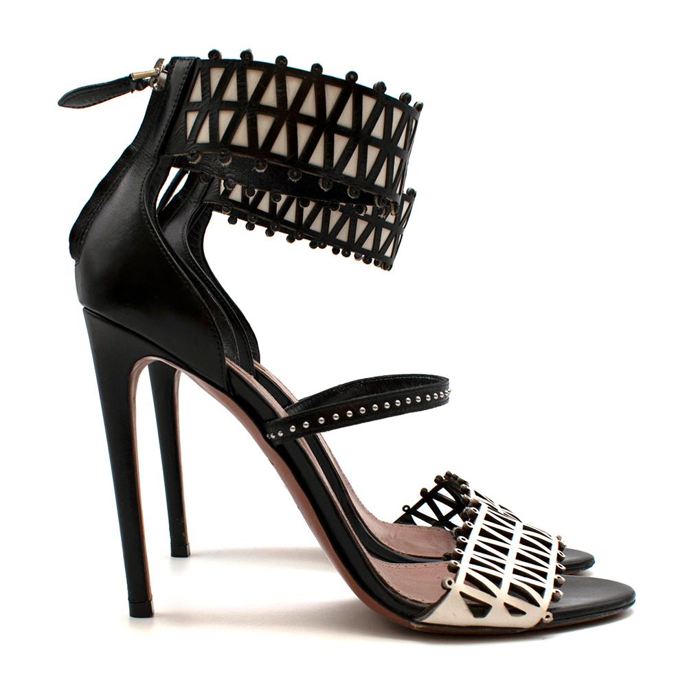 Alaia Stiletto Black & White Lasercut Sandals

- Size 40 = UK 7
- Laser cut design on the front of the toes
- Large ankle strap with white leather contrast
- Mid ankle strap with silver studs
- Back zip attachment with silver hardware
- Tall