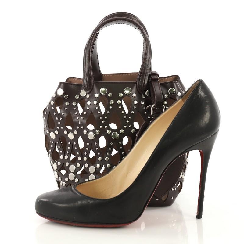 This Alaia Studded Bucket Bag Laser Cut Leather Mini, crafted in brown laser-cut leather, features dual leather handles, stud detailing and silver-tone hardware. It opens to a nude leather interior. **Note: Shoe photographed is used as a sizing