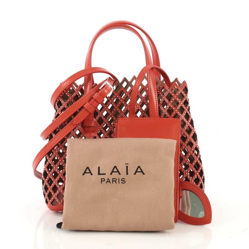 This Alaia Studded Open Tote Laser Cut Leather Small, crafted from red laser cut studded leather, features dual leather handles, side snap buttons, and silver-tone hardware. It opens to a beige laser cut leather interior.

Estimated Retail Price: