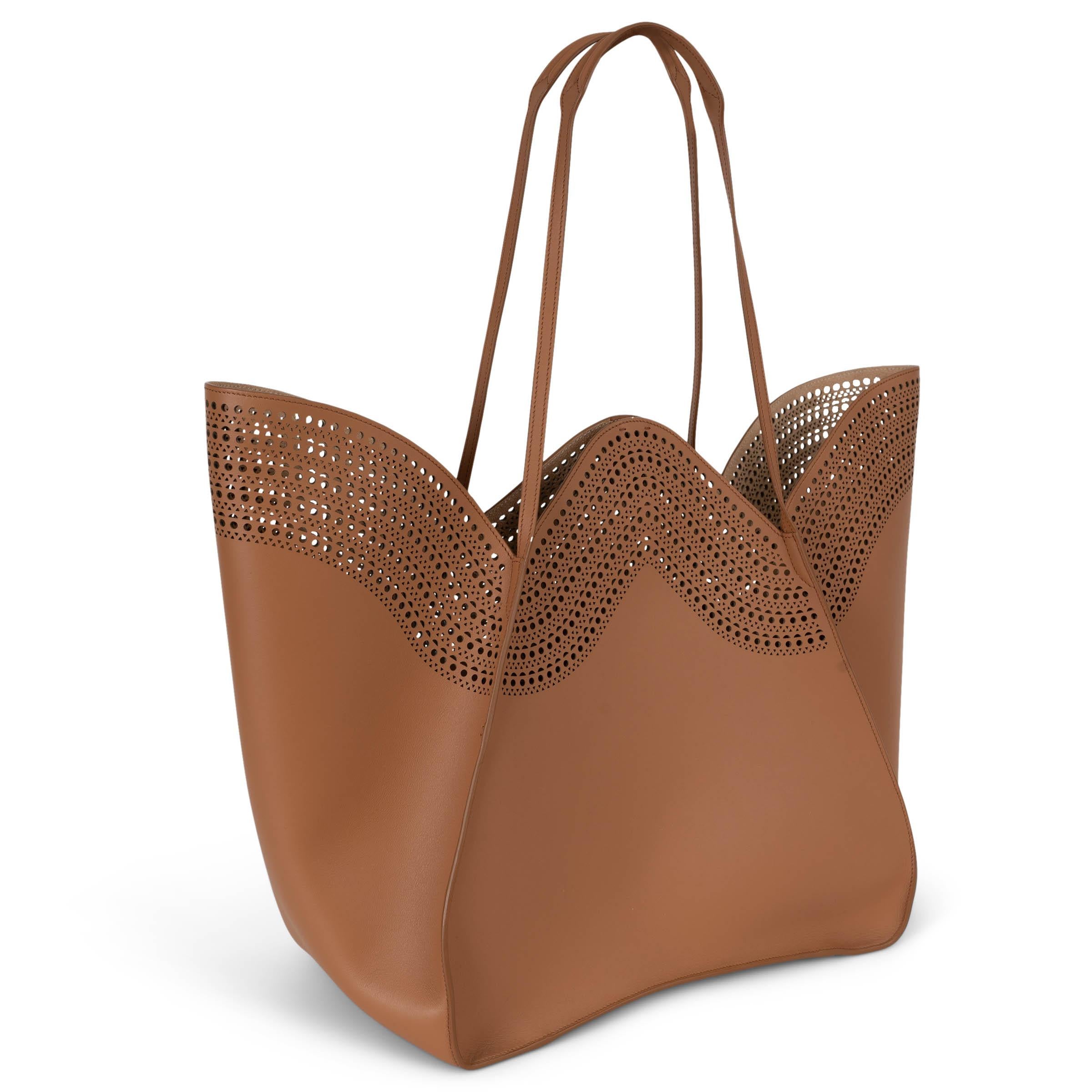 This 100% authentic Alaïa Lili 32 tote in tan brown leather showcases the brand’s signature craftsmanship with intricate laser-cut Vienne perforation. Designed with a delicate flower-inspired silhouette, it features a scalloped top edge and double