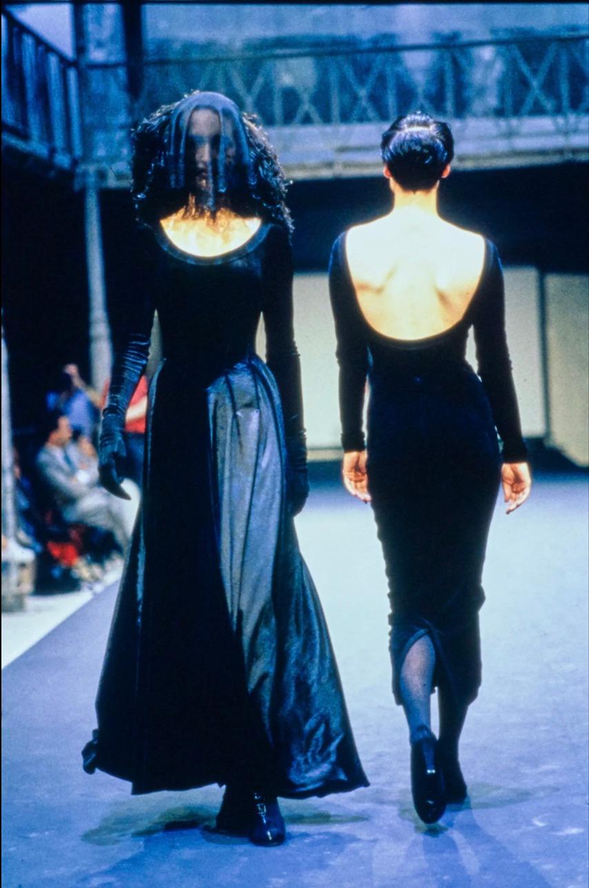 Ti presentiamo il body in velluto nero di Alaia della collezione Autunno/Inverno 1988. Vanta un profondo scollo a palloncino che incornicia elegantemente il décolleté, completato da un raffinato bordo in maglia. Il design è caratterizzato da una