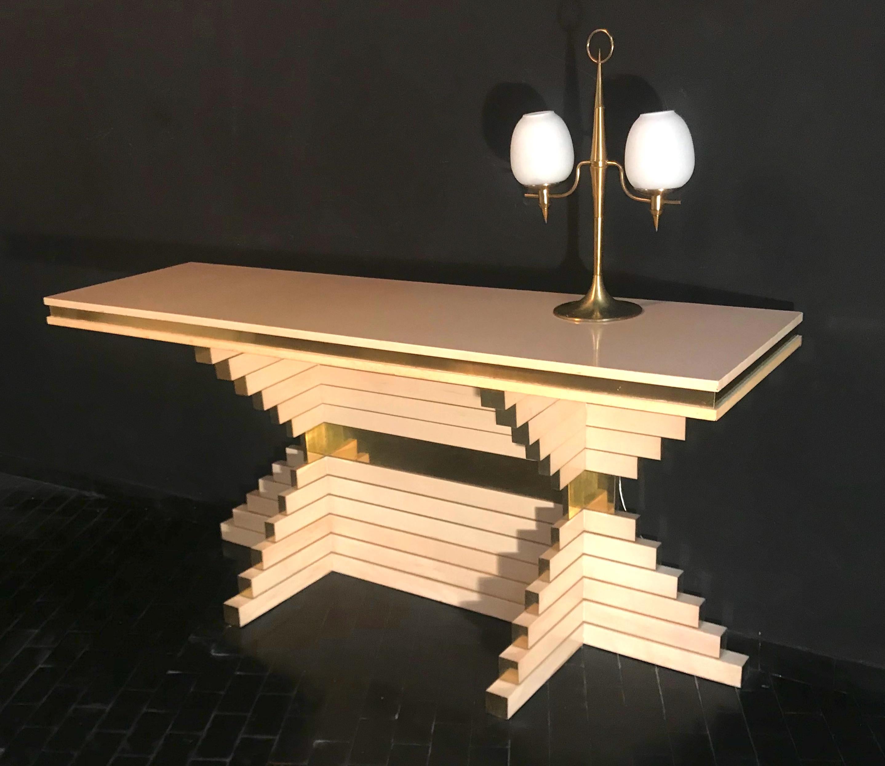 One of a kind outstanding console table designed by Alain Delon for Maison Jansen, it features a skyscraper style silhouette with its gorgeous stacked obtuse form. This console features ivory lacquer finish with brass banding and