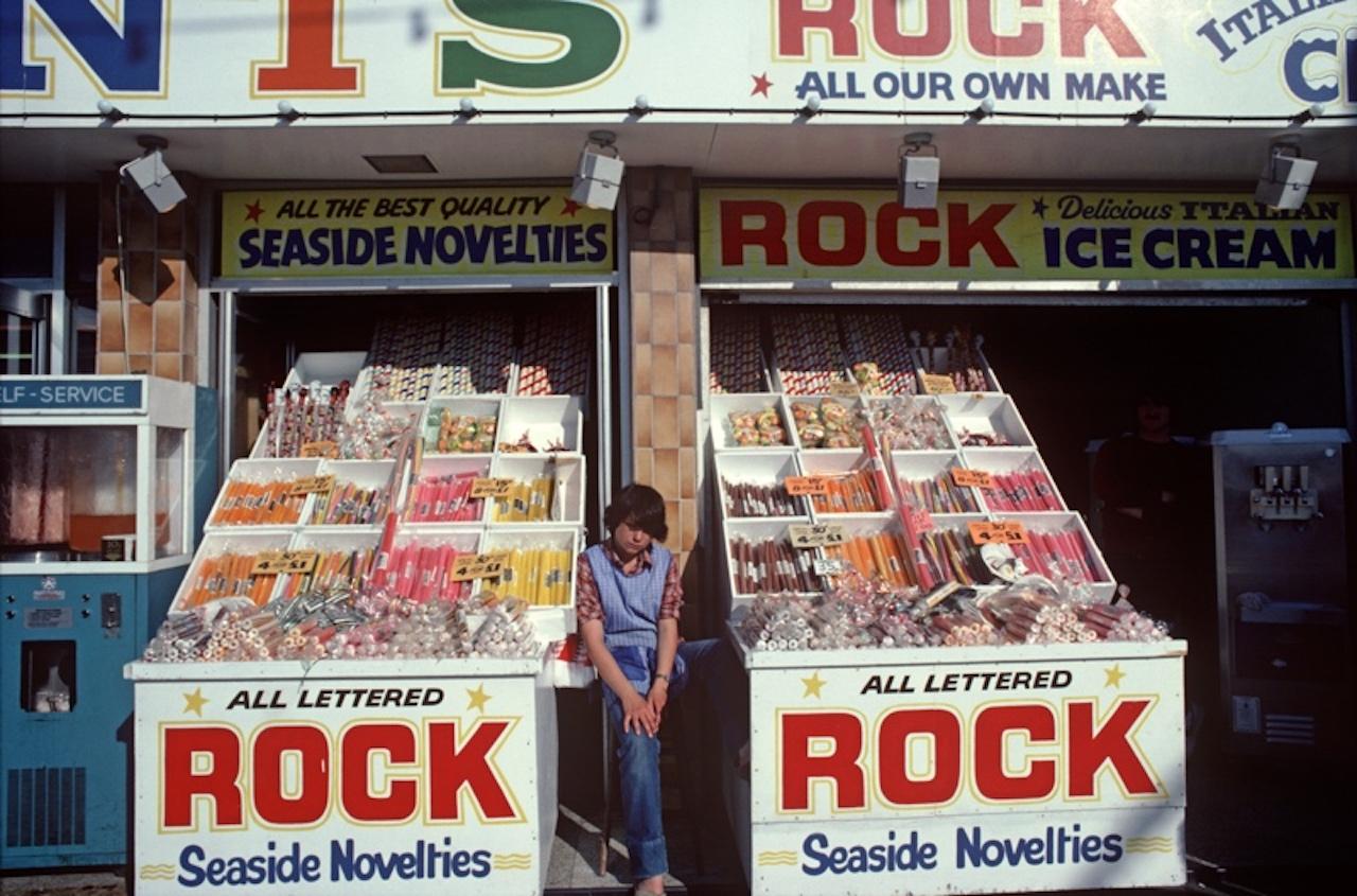 Rock On At The Seaside von Alain Le Garsmeur
Ein Geschäft, das Rock- und Strandartikel entlang der Golden Mile verkauft, Blackpool, England, 1981. 

Papierformat 20 x 24 Zoll / 50 x 60 cm
Gedruckt im Jahr 2022 - hergestellt von der
