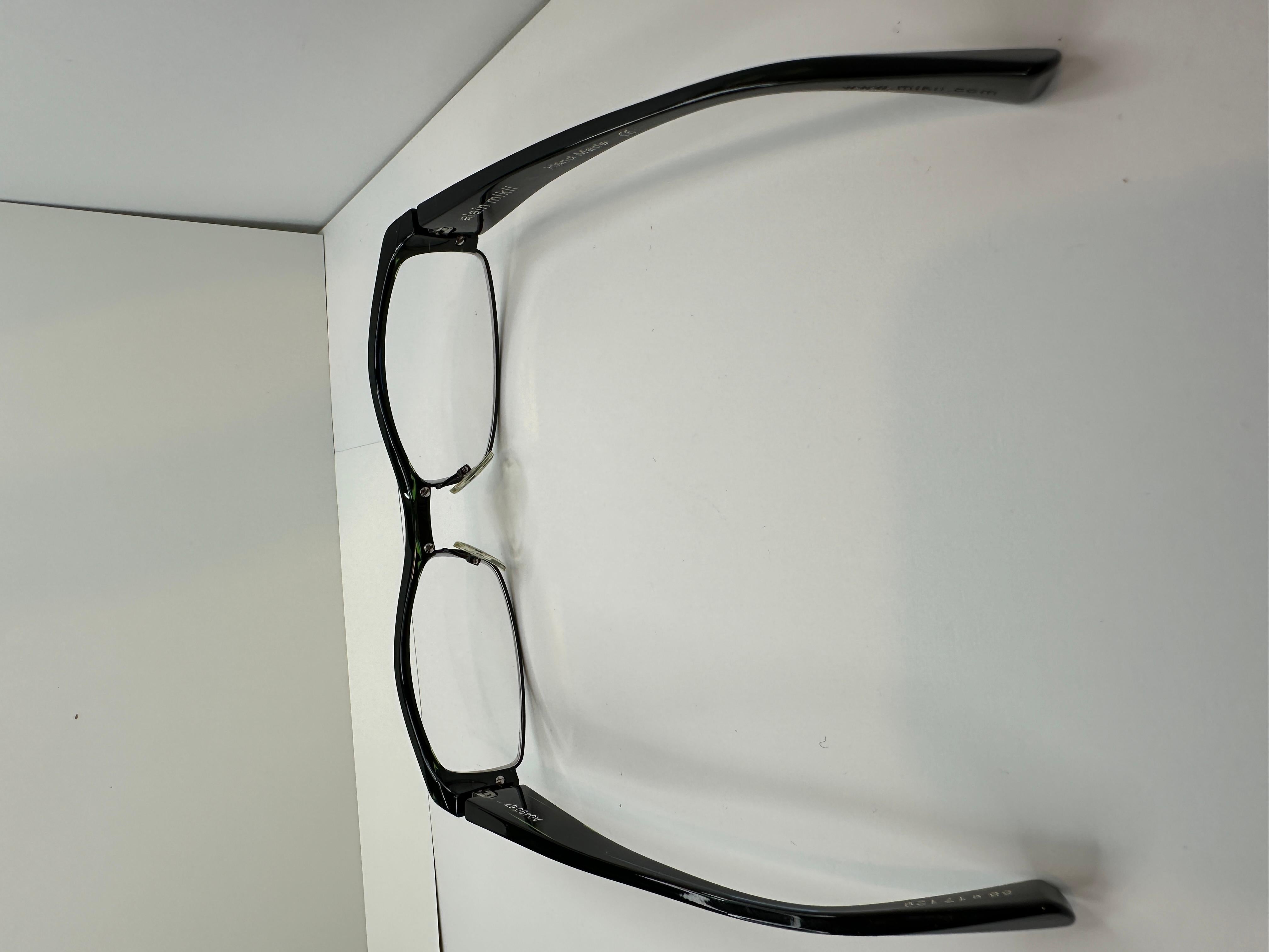 Alain Mikli thick black lucite prescription frames accented with clear green stripes along the arms are hand-made in Japan. The length across the front measures 5 1/2 inches, height is 1 1/4 inches, arm's length measures 5 2/16 inches. 