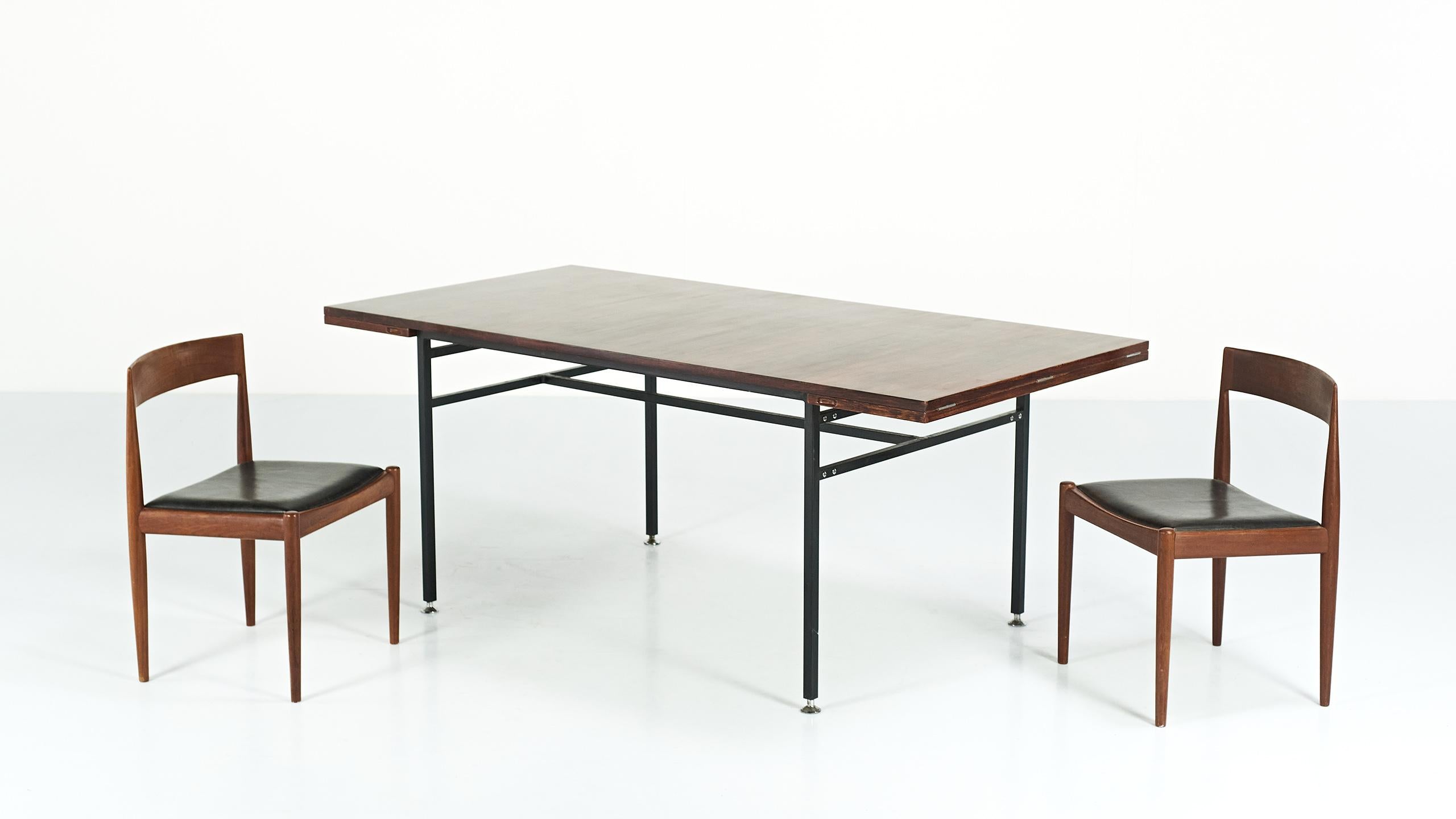 Modernist dining table, by French designer Alain Richard and manufactured by Meubles TV during the 50’s. It consist on a walnut veneered table top, with two extensions, supported by a black lacquered square shaped tubular steel base, enhanced by