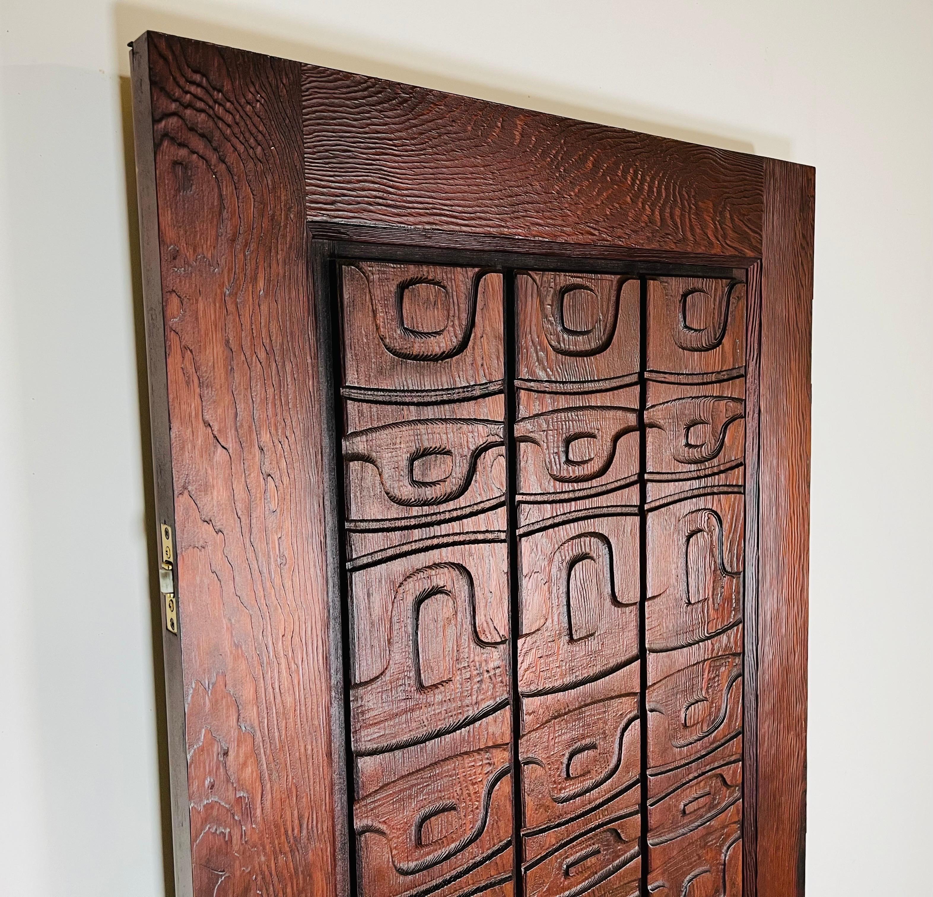 A masterpiece studio carved front or outer door. Hand carved redwood by an Alaskan artist from either the Tlingit or Cup'ik tribe and imported in 1971 by its original and only owner. Adorned with solid bronze matching door pulls having a matching