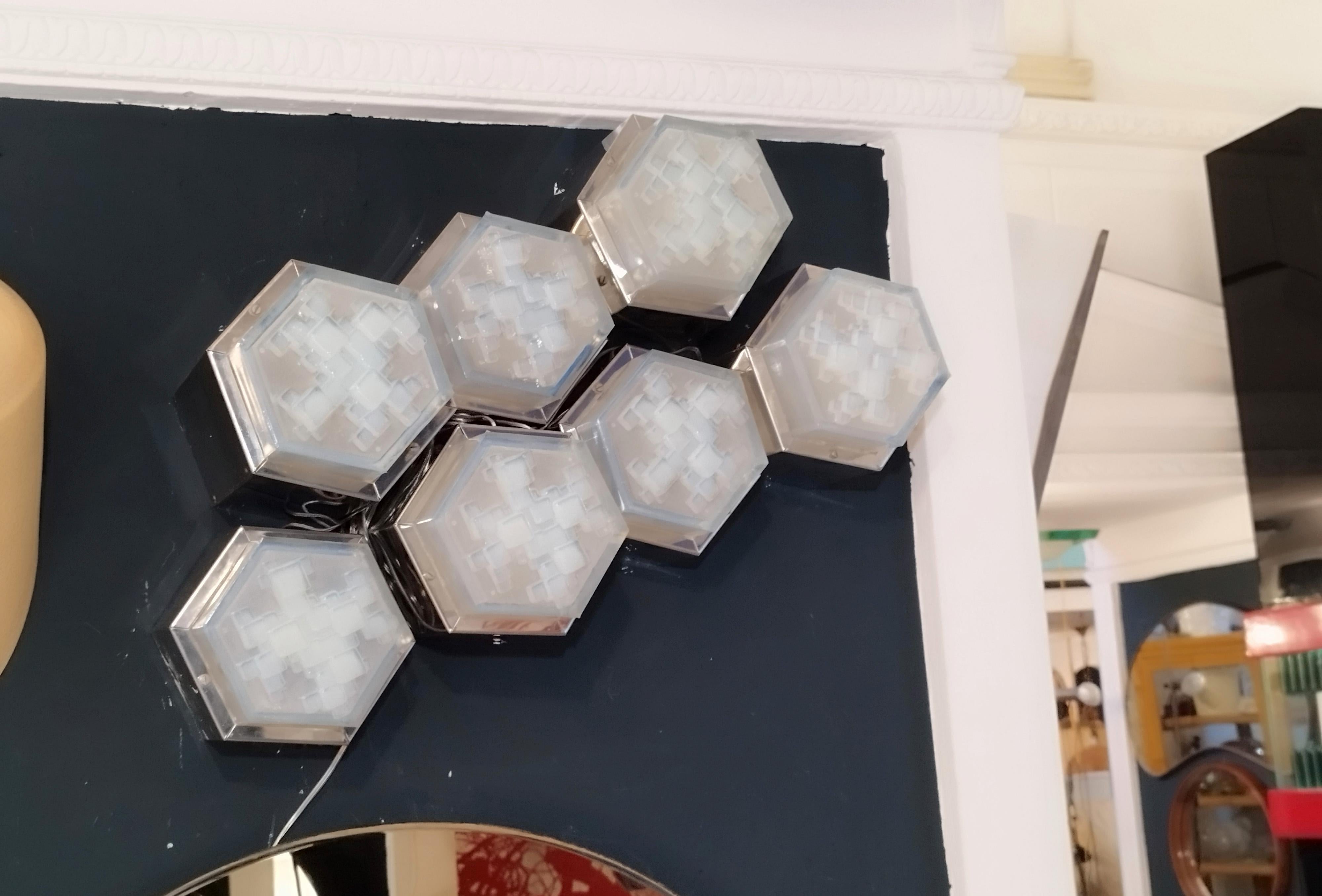 Appliques murales ou encastrées modulaires avec cadre hexagonal en acier et diffuseur hexagonal en verre bleu givré, conçues par Albano Poli pour Poliarte.
L'ensemble se compose de 7 lampes de différentes tailles :
1 lampe cm. h.21x18x14
3 lampes