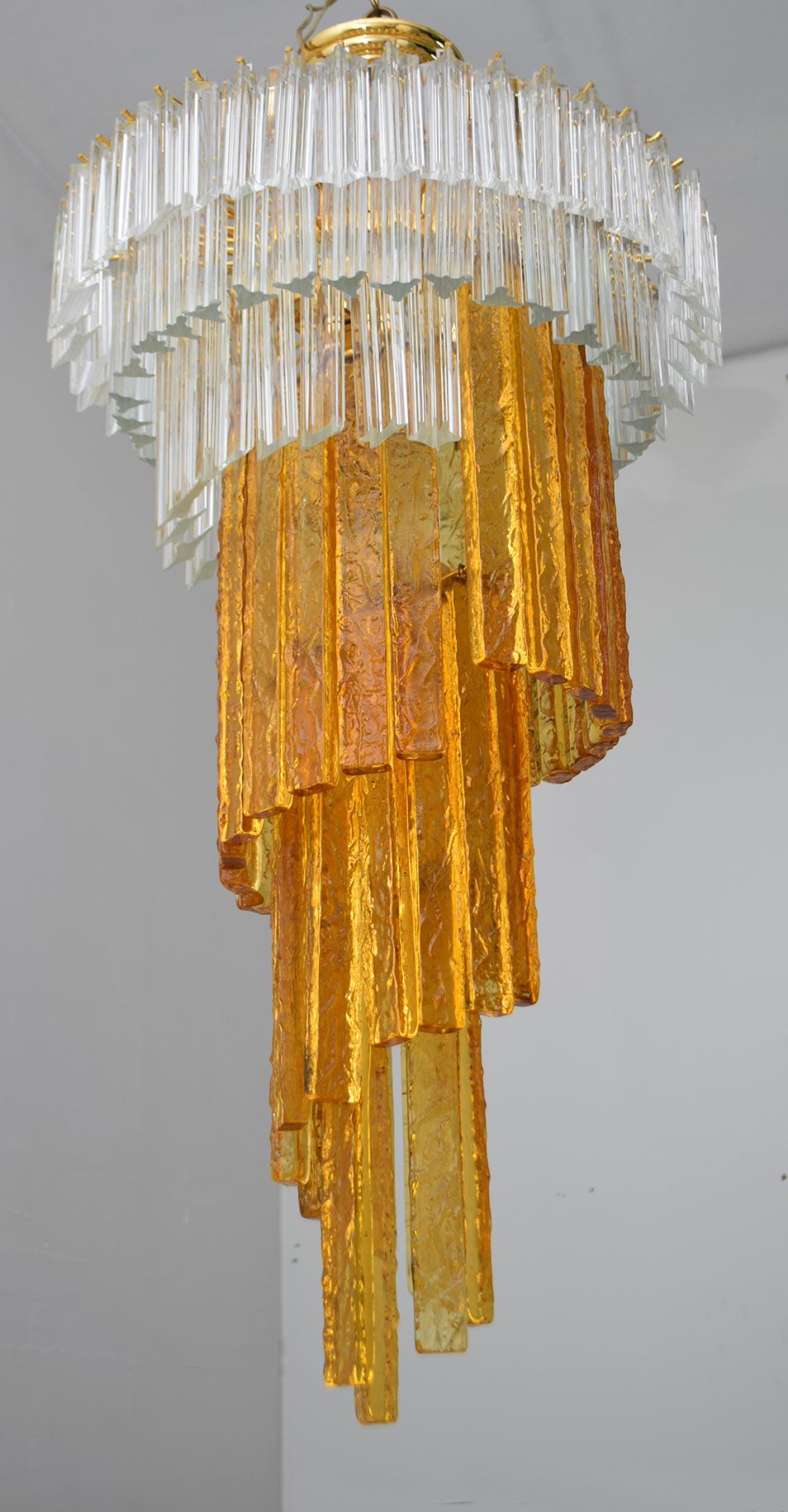 This chandelier was created by master glassmaker Albano Poli for his company Poliarte. Eight lights chandelier, with structure in gold chromed metal, amber Murano glass parallelepipeds and trihedrons and transparent Murano crystal panels, to create
