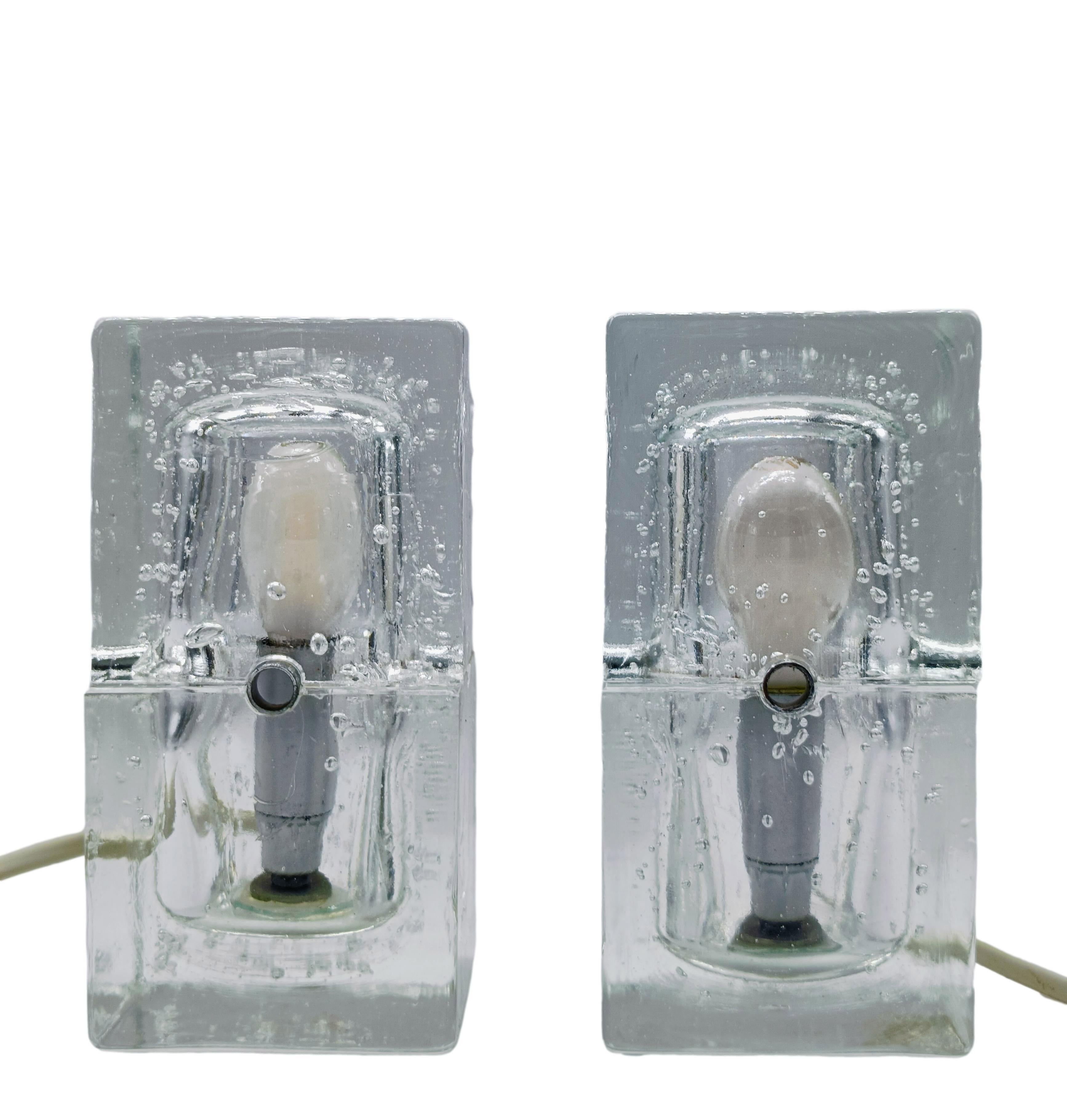Questa coppia di lampade risale al 1970 ed è stata realizzata in Italia. Si tratta di un cubo di vetro di Murano in due parti con una cavità cilindrica in cui vengono inserite le lampadine. È montato su una piastra di metallo ed è in buone