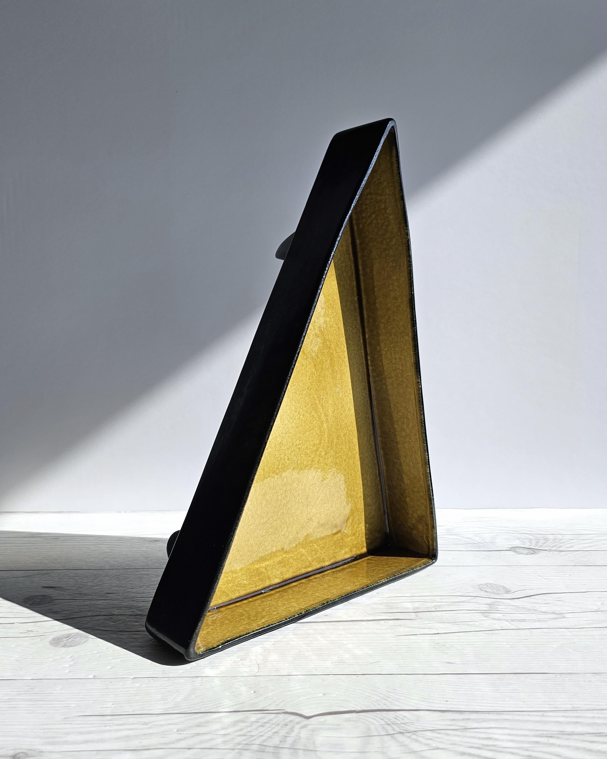 Cette œuvre subtilement audacieuse d'influence moderniste est l'œuvre du designer et modéliste Albert Hallam.  La forme surélevée et tranchante du triangle droit de cette pièce attire l'attention par sa présence et il est difficile de l'éviter où