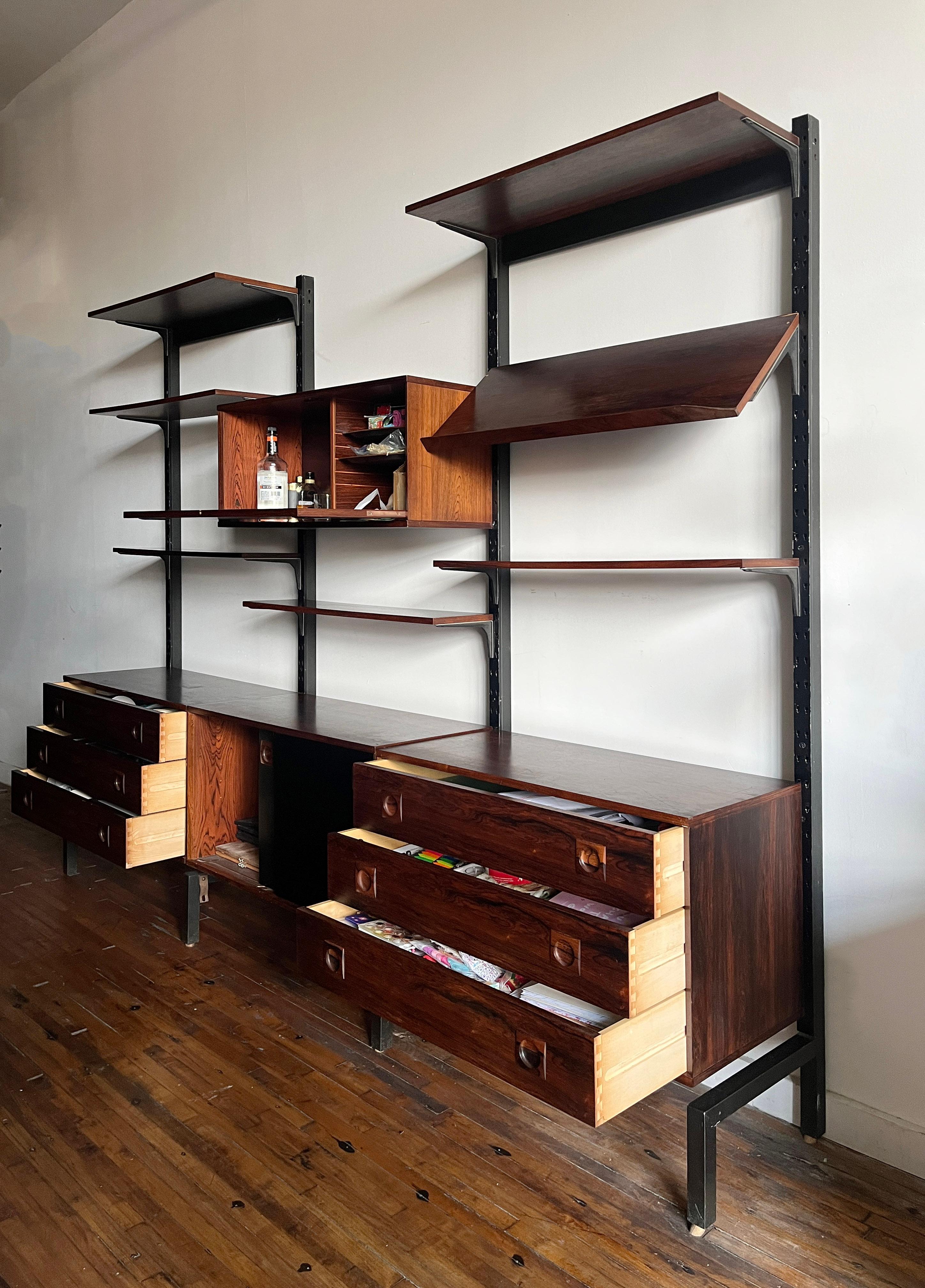 This is one beautiful Brazilian rosewood Danish shelving modular system by Albert Hansen 1980s (Signed). This unit includes 7 shelves, 1 slanted book display, 1 drop down door dry bar, 1 double door sliding cabinet, 2 cabinets with three drawers