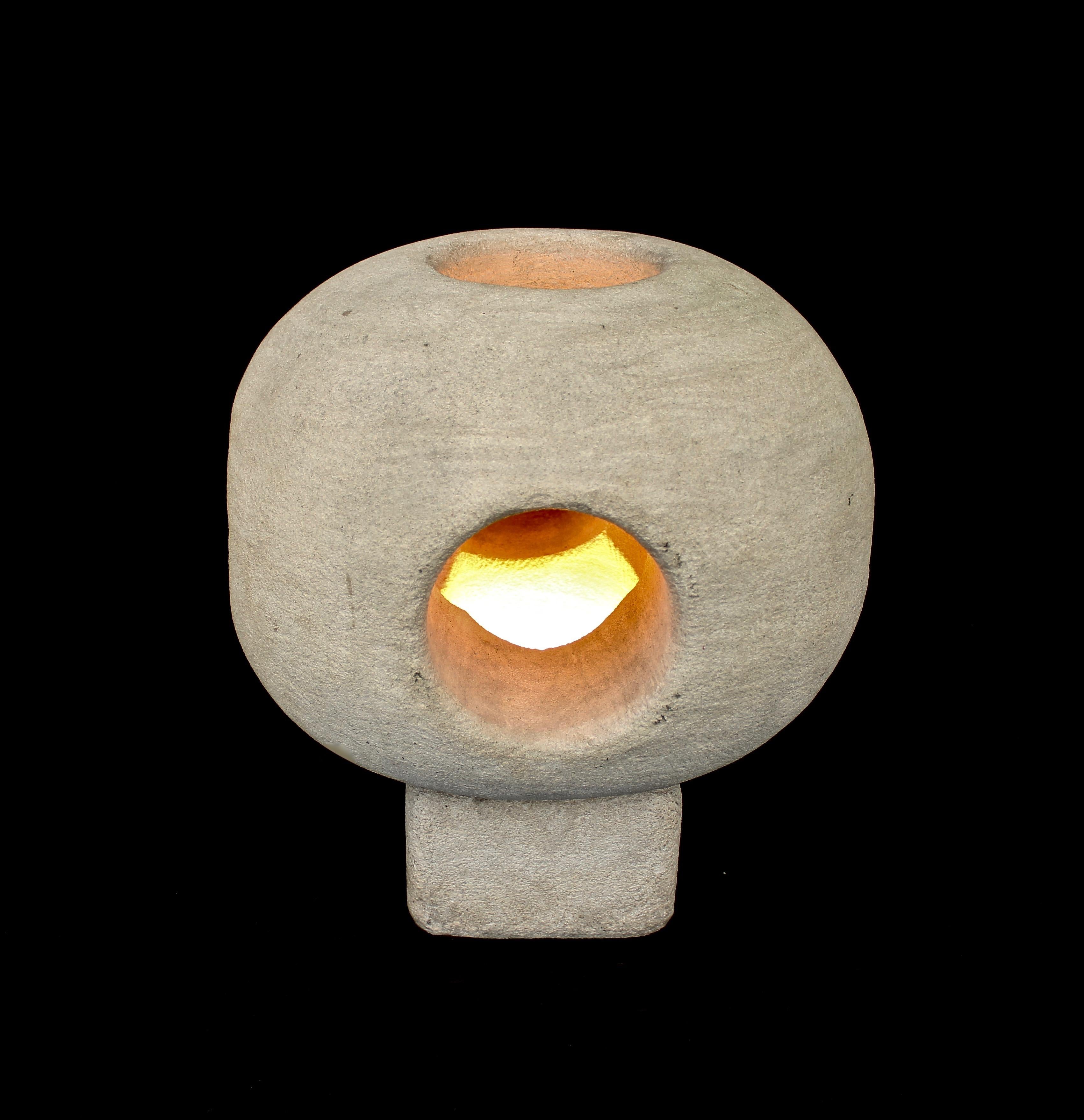 A solid carved French limestone sculptural table lamp by Albert Tormos.
The lamp is a porous French buffa or limestone that is hand carved into a round top with openings on each and top for the light to emit a soft glow.
Upon close viewing the