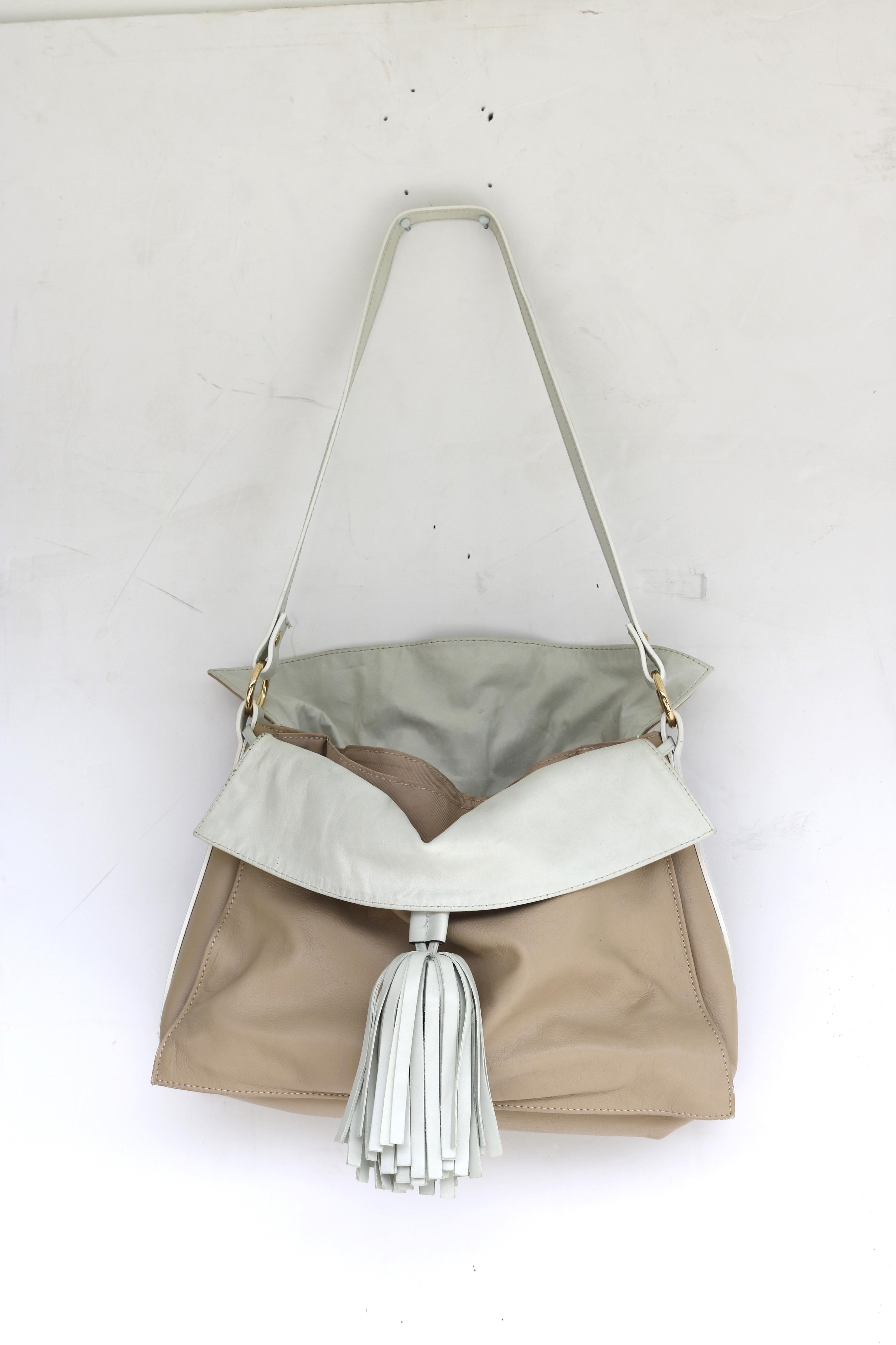 Stylish Fine Beige Leather with Large Oyster White Leather Tassel and leather  fold over front and back flaps Slouch Shoulder Handbag- gold tone hardware, magnetic closing.  Made in Italy- circa 1980s.
A chic Valentino style handbag with slouchy