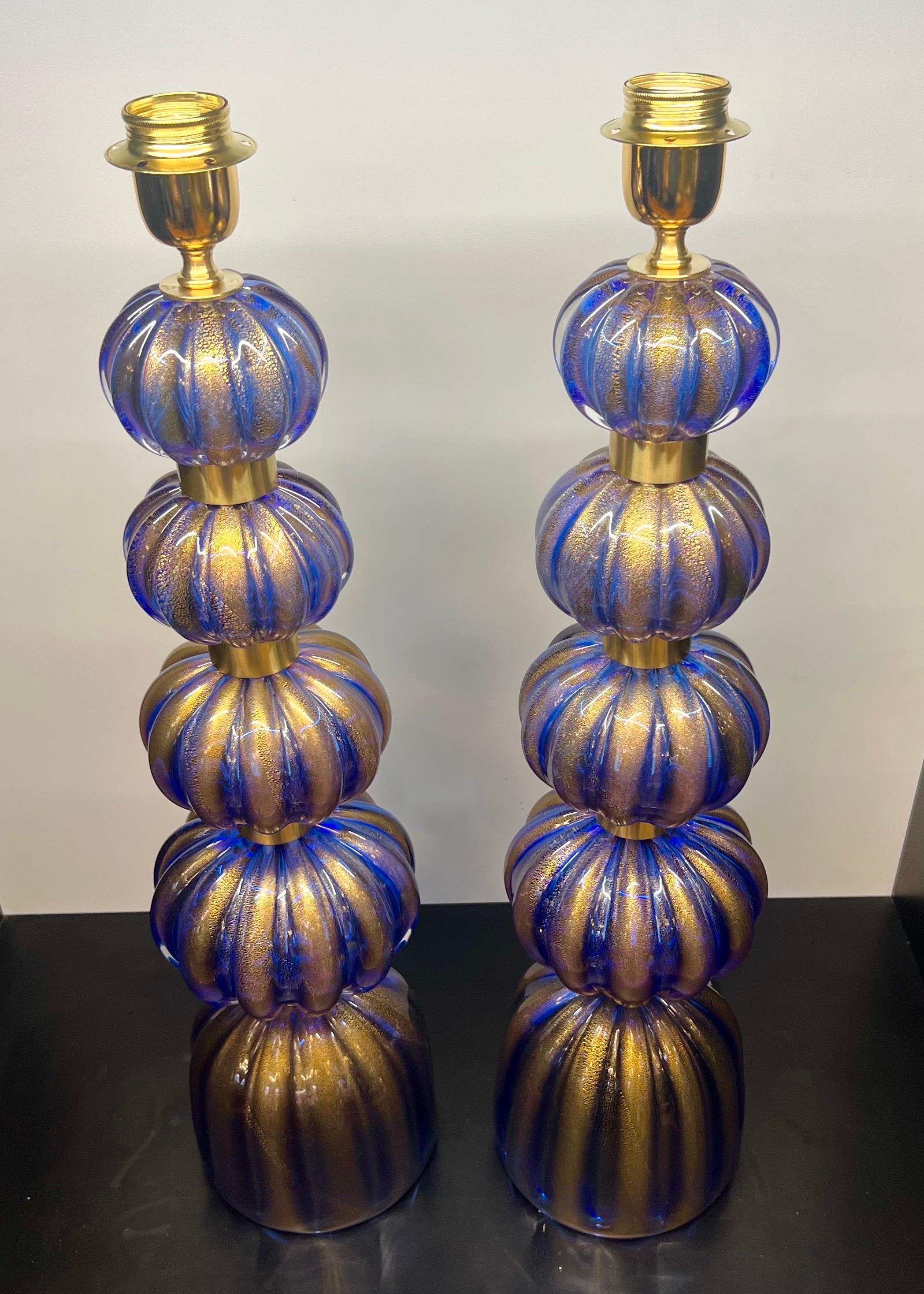 Paire exclusive de lampes de table en verre bleu de Murano avec monture en bronze satiné.
La lampe est composée de 4 éléments en forme d'oignon et d'un élément qui fait office de base en forme de cloche, le tout en feuille d'or 24 carats.
En