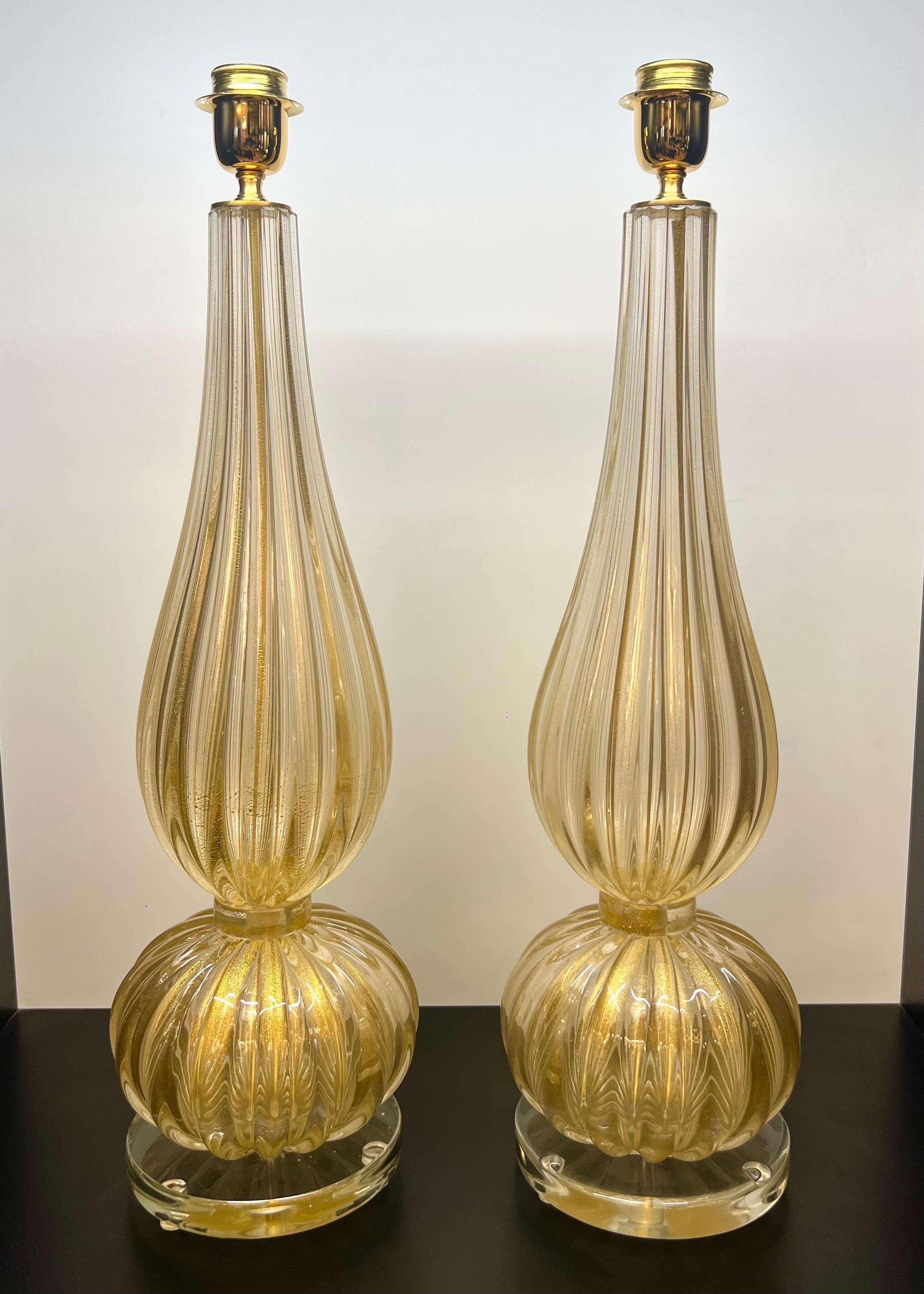 Paire exclusive de lampes de table en verre de Murano 24 carats avec feuille d'or et monture en bronze satiné.
La lampe est composée d'un élément en forme d'oignon et d'un élément en forme de goutte.
En touchant la lampe de la main, vous remarquerez