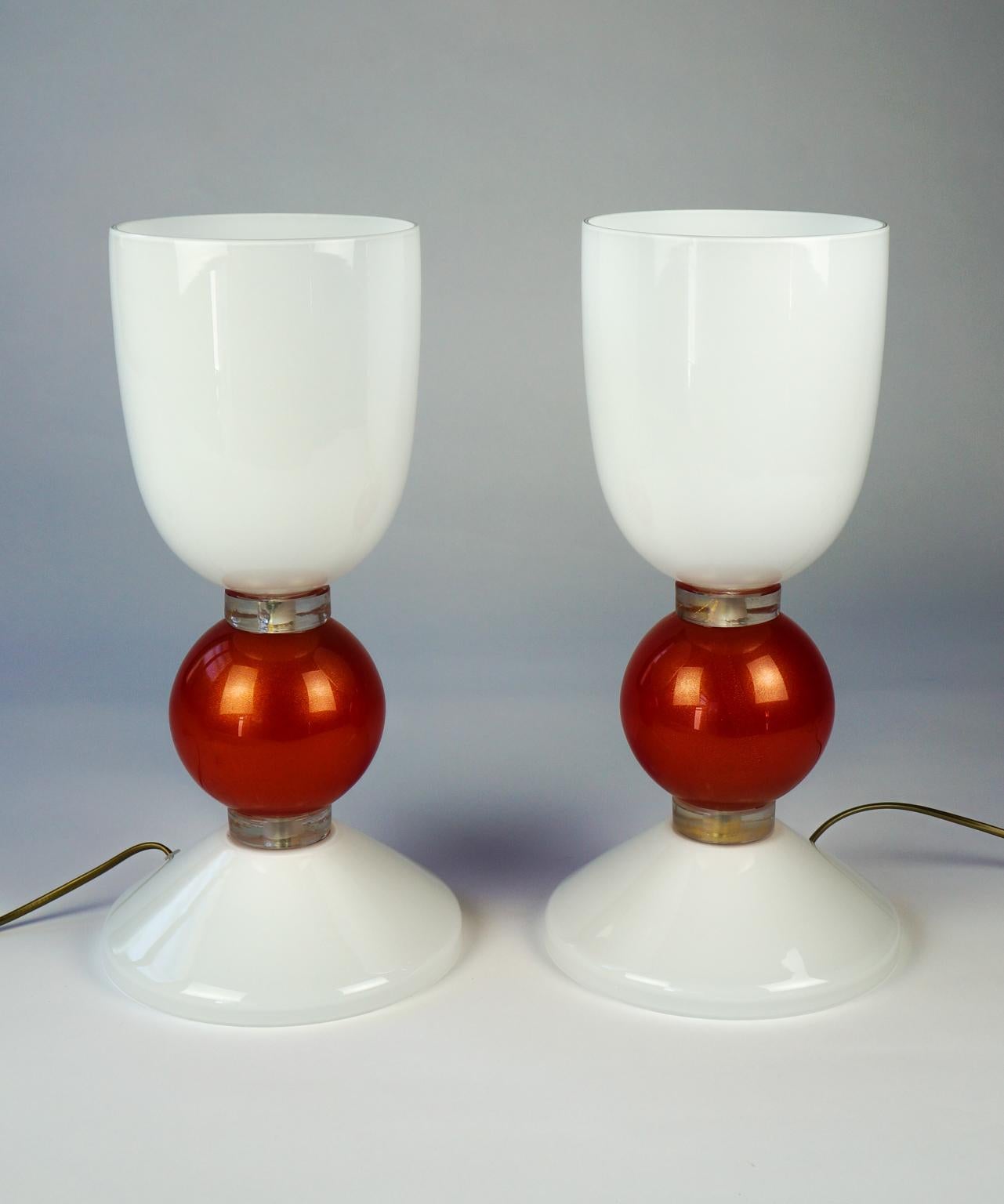 Designed in 1984, this lamp is composed of a milky white base, which recalls the color of the cup. There, a light bulb is inserted that gives off a very soft light thanks to the opacity of the white Murano glass. The two pieces are joined by a red