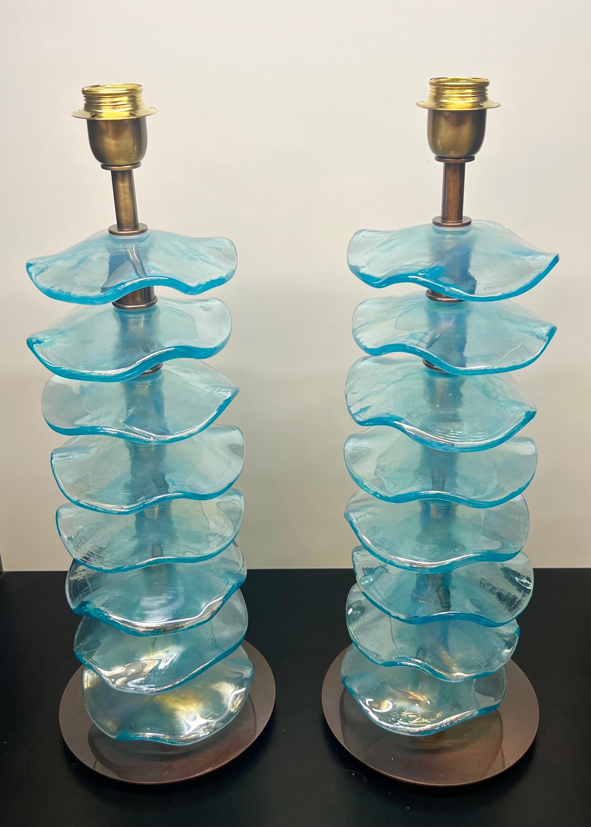 Esclusiva coppia di lampade da tavolo in vetro di Murano azzurro con montatura in bronzo satinato.
La lampada è composta da 8 elementi di forma circolare ondulata di colore azzurro specchiato.
Lampada realizzata con grande cura e precisione dal