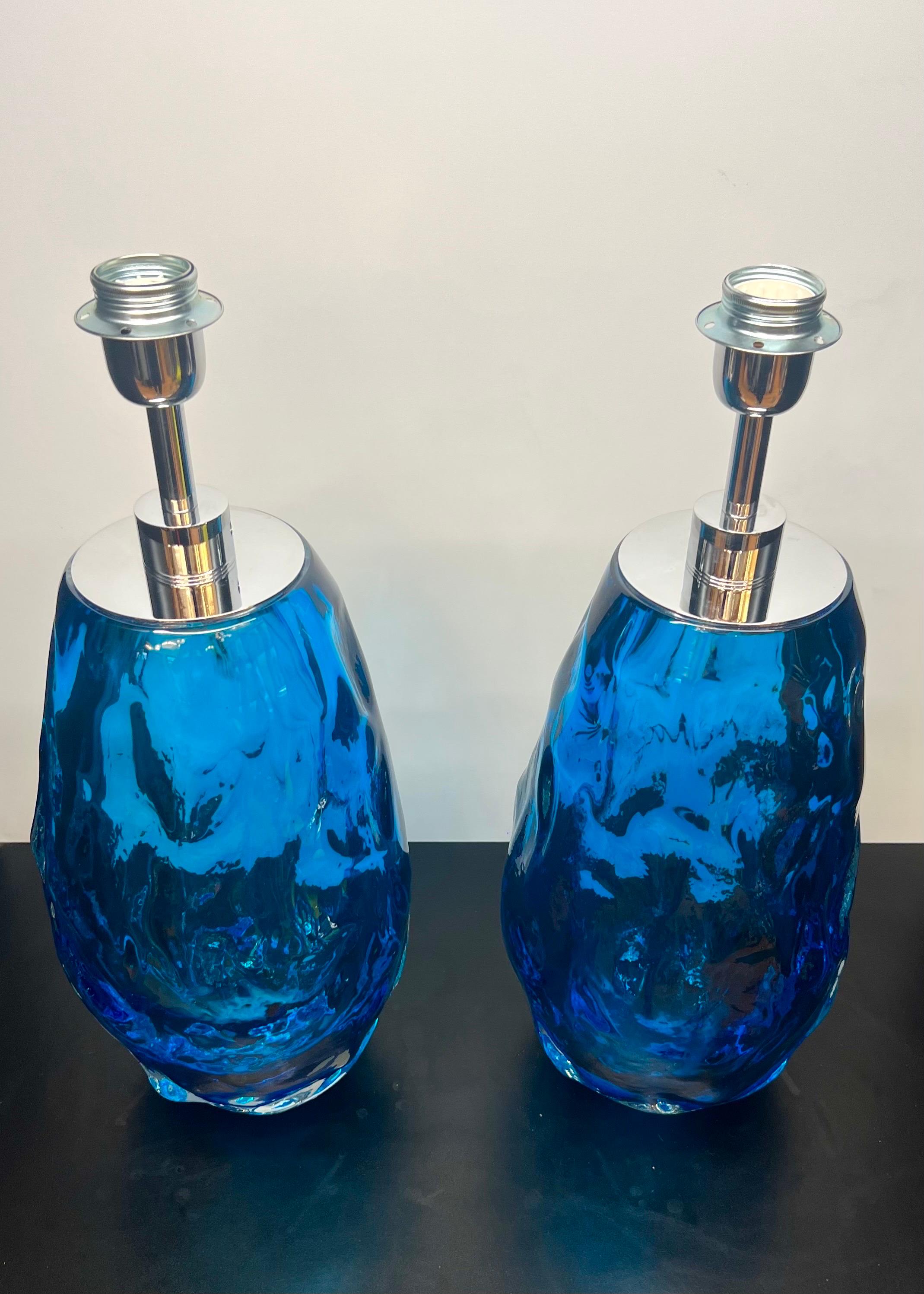 Exclusivo par de lámparas de mesa de cristal de Murano azul claro con marco de cromo pulido.
La lámpara está compuesta por un único elemento de vidrio soplado grueso trabajado para que parezca una roca, este proceso se denomina 